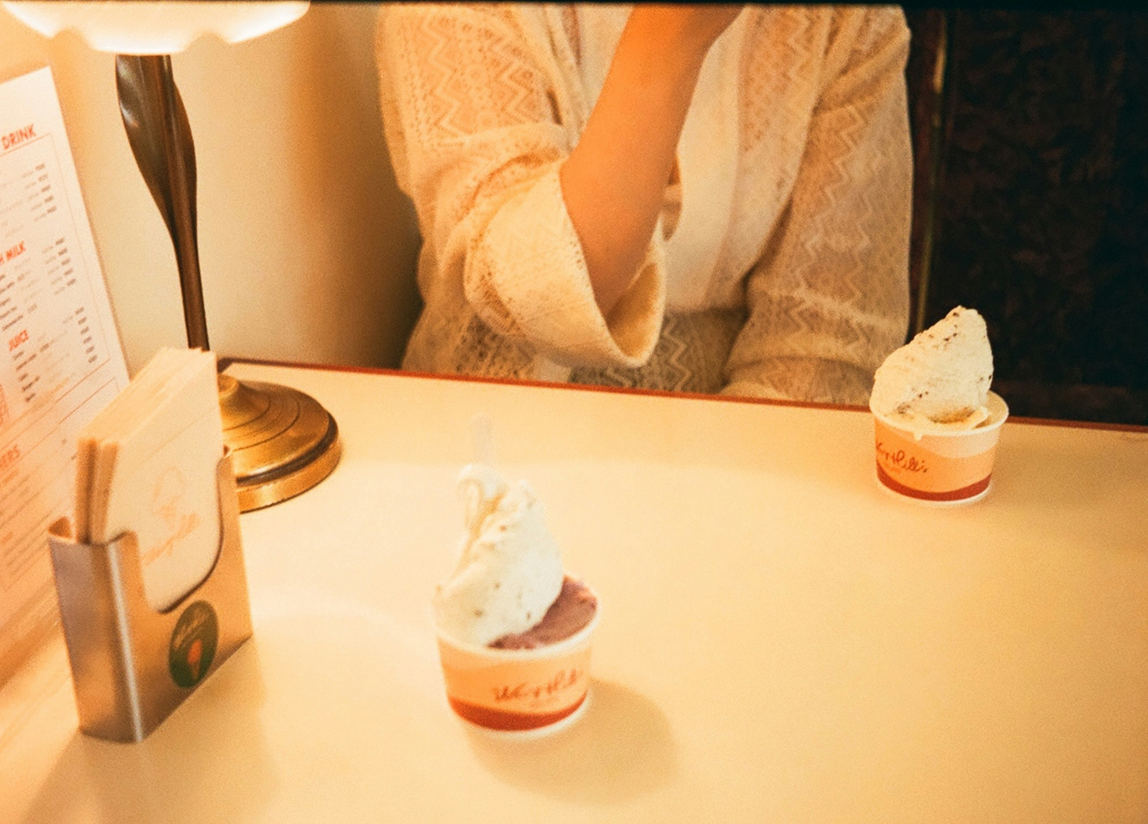 Dos copas de helado en una mesa con una mujer llevándose la mano a la boca