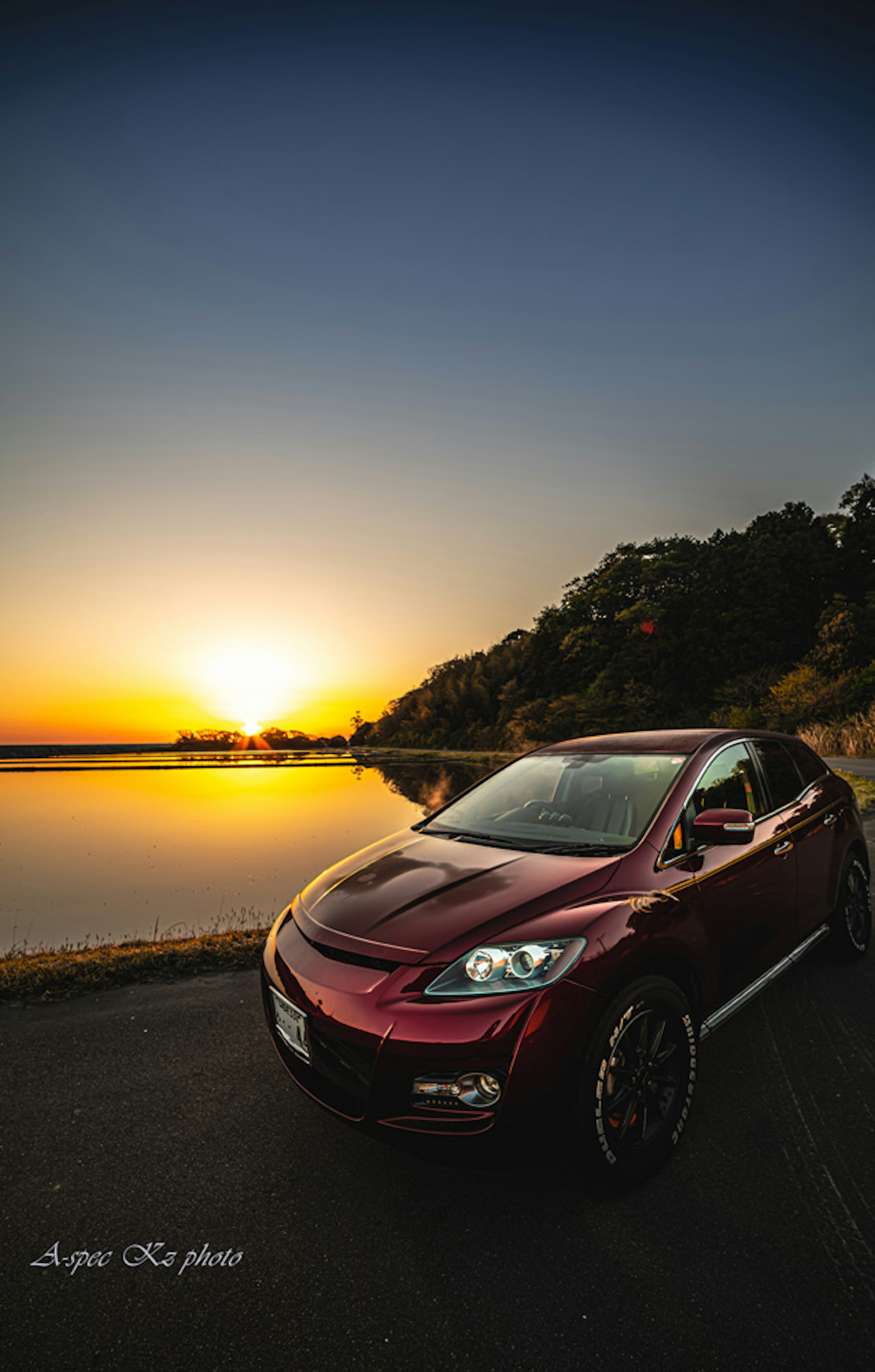 A red car parked near a lake with a sunset backdrop