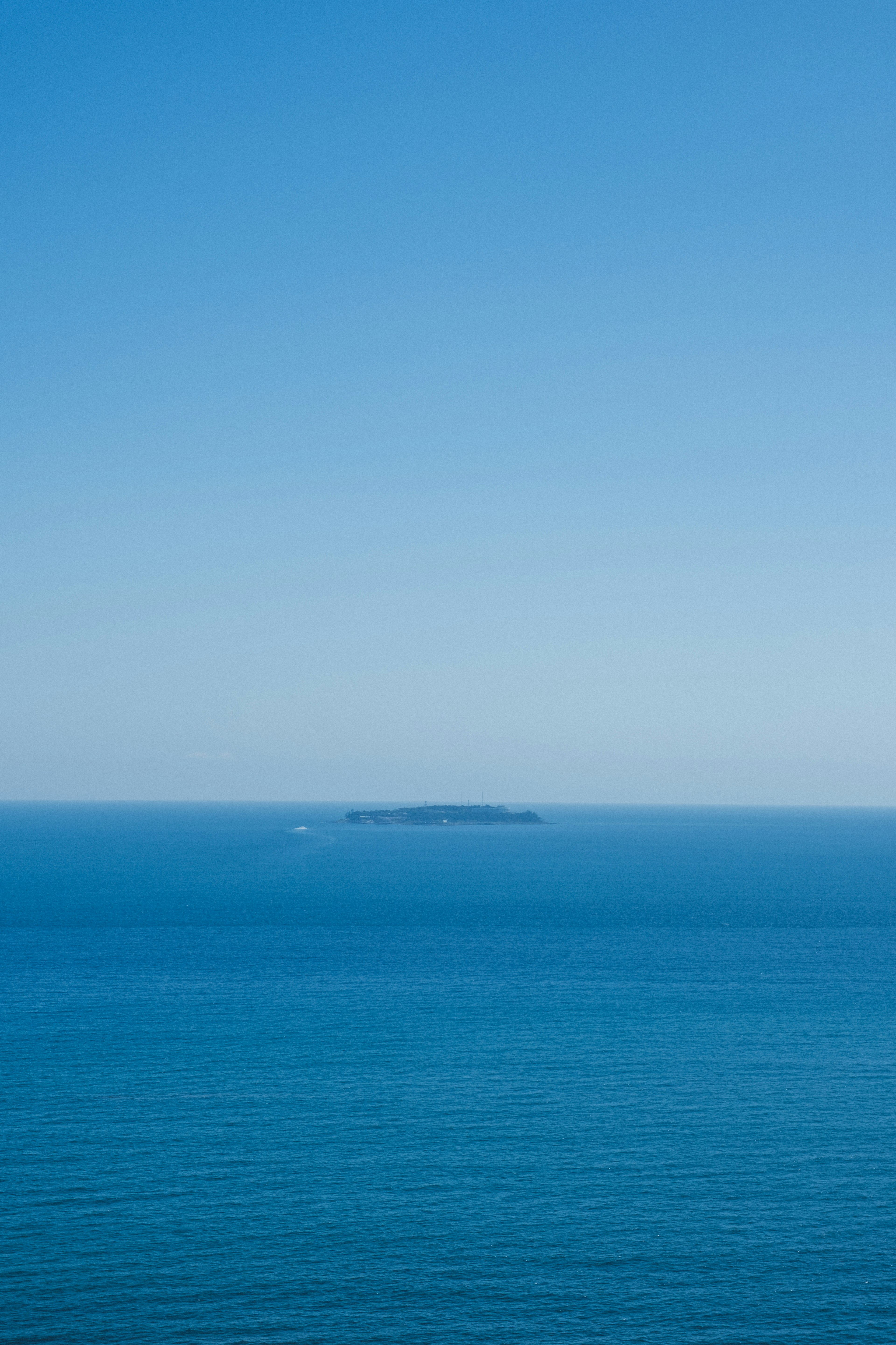 Una piccola isola visibile in una vasta distesa di oceano e cielo blu