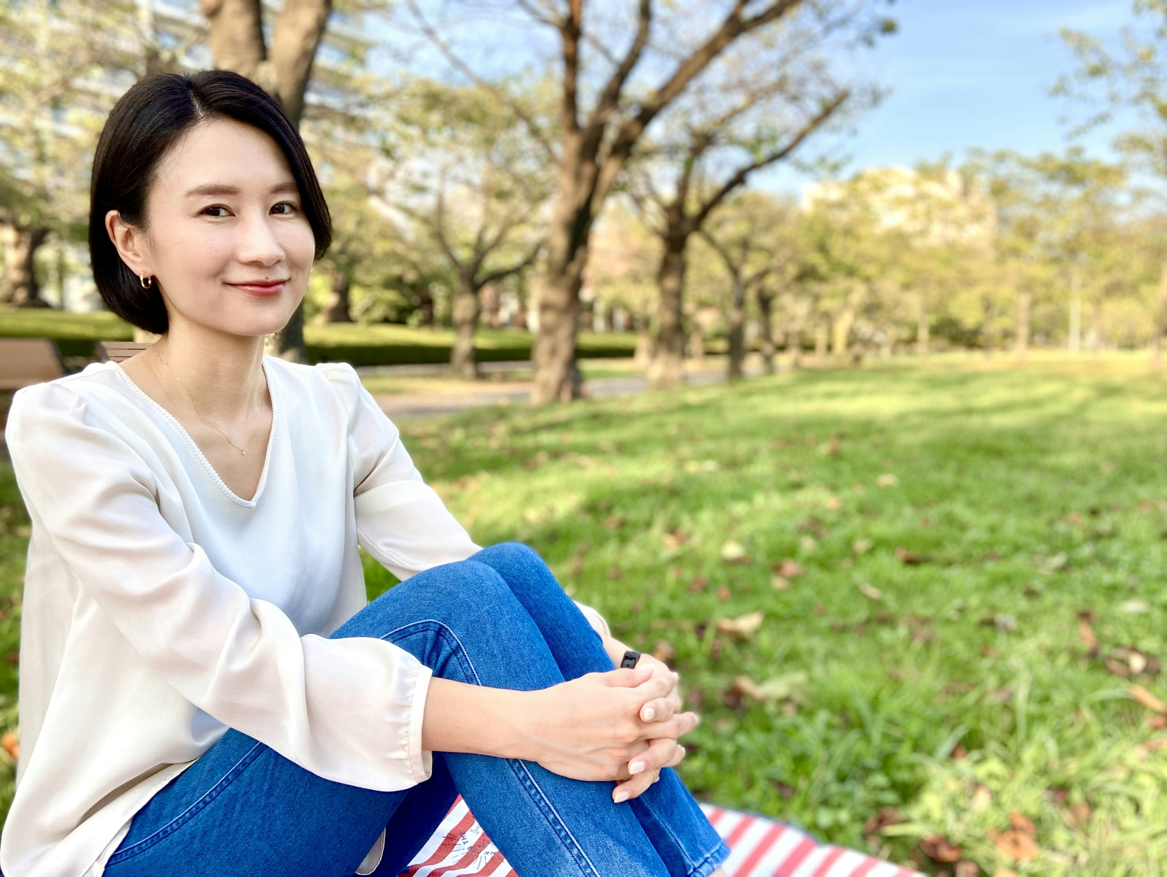 Wanita bersantai di taman mengenakan jeans biru dan atasan putih dengan senyuman