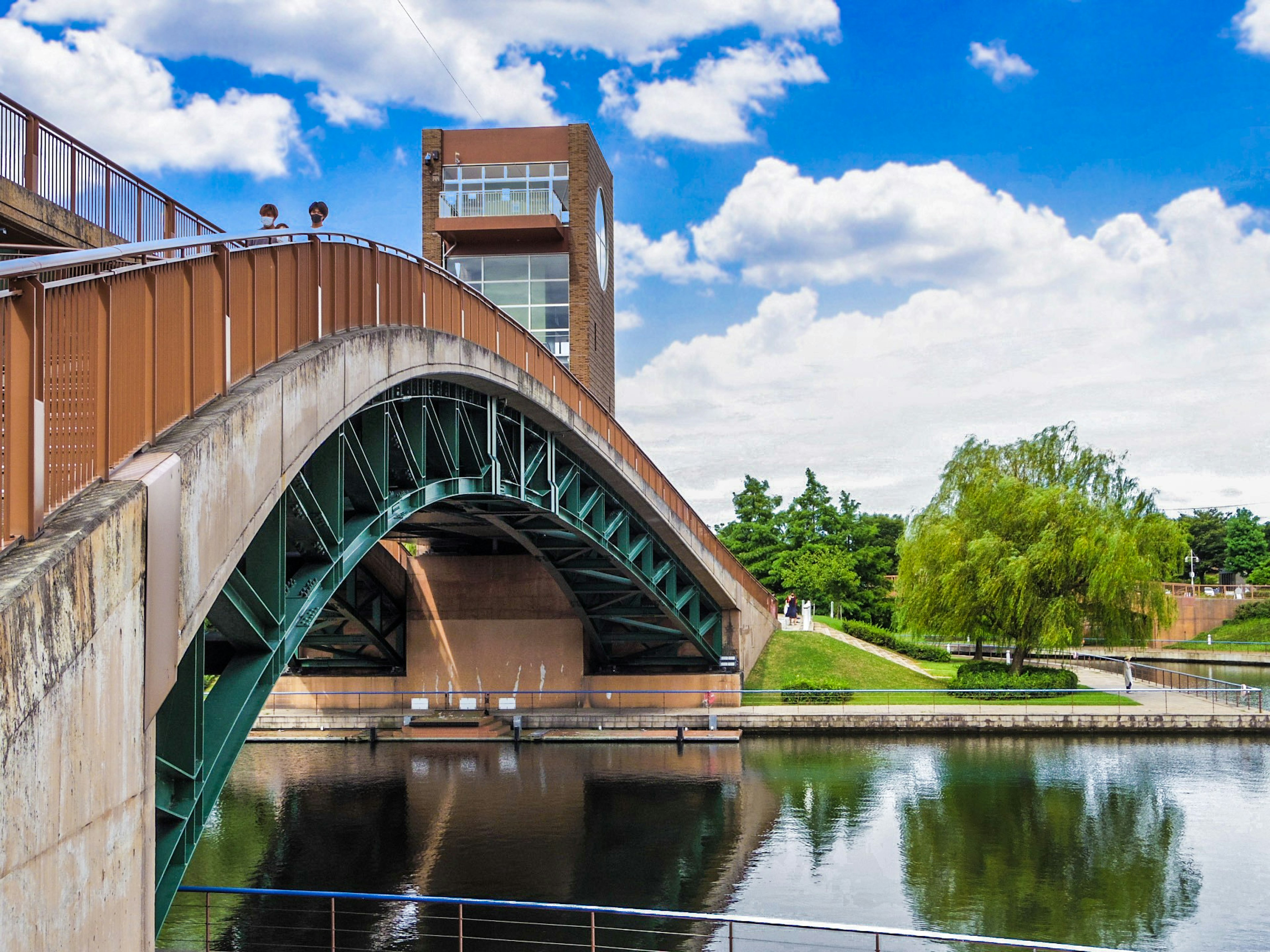 Grüner Bogenbrücke über ruhigem Wasser mit blauem Himmel und weißen Wolken