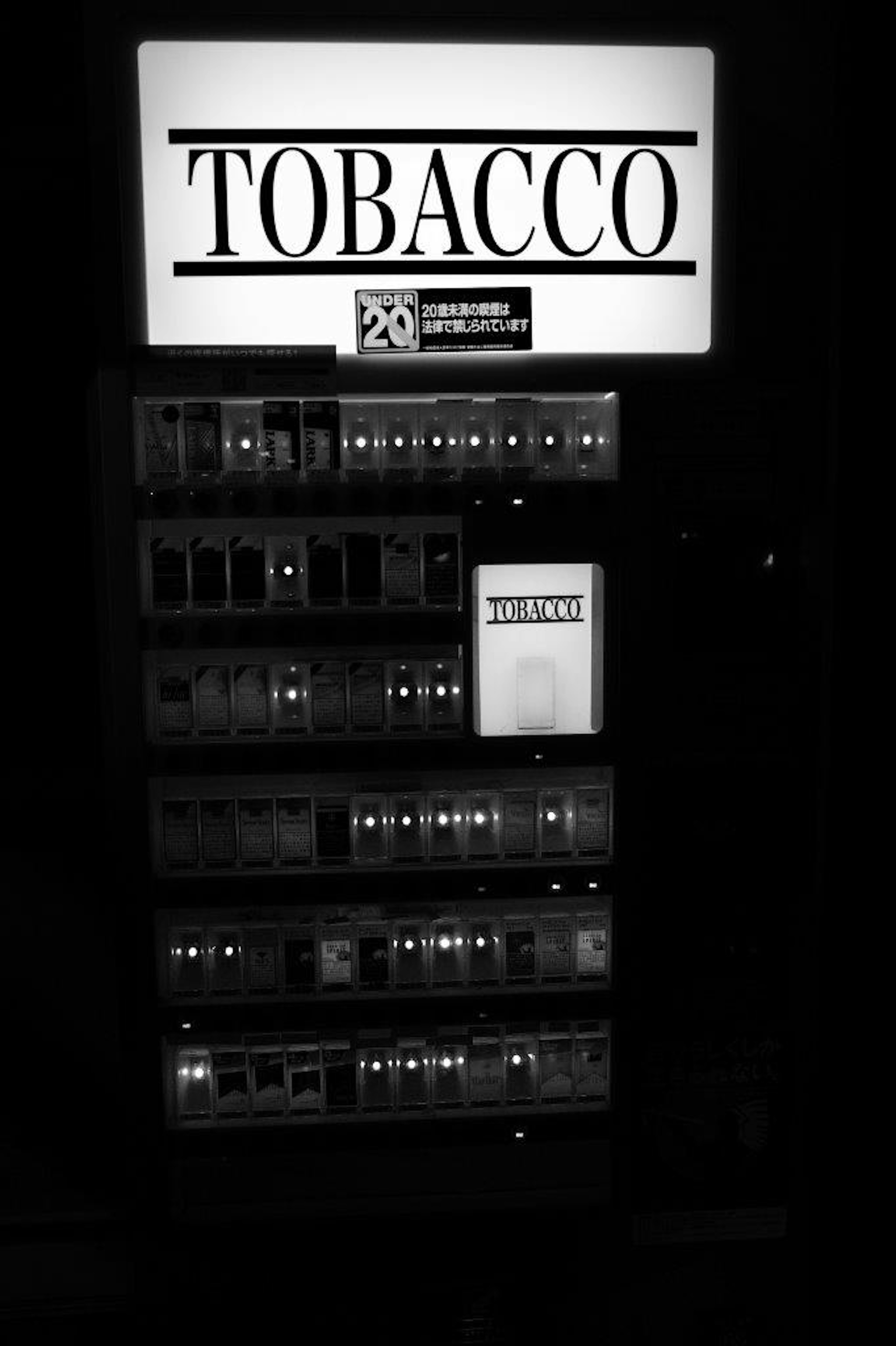 Black and white image of a tobacco vending machine featuring the word Tobacco and various product options