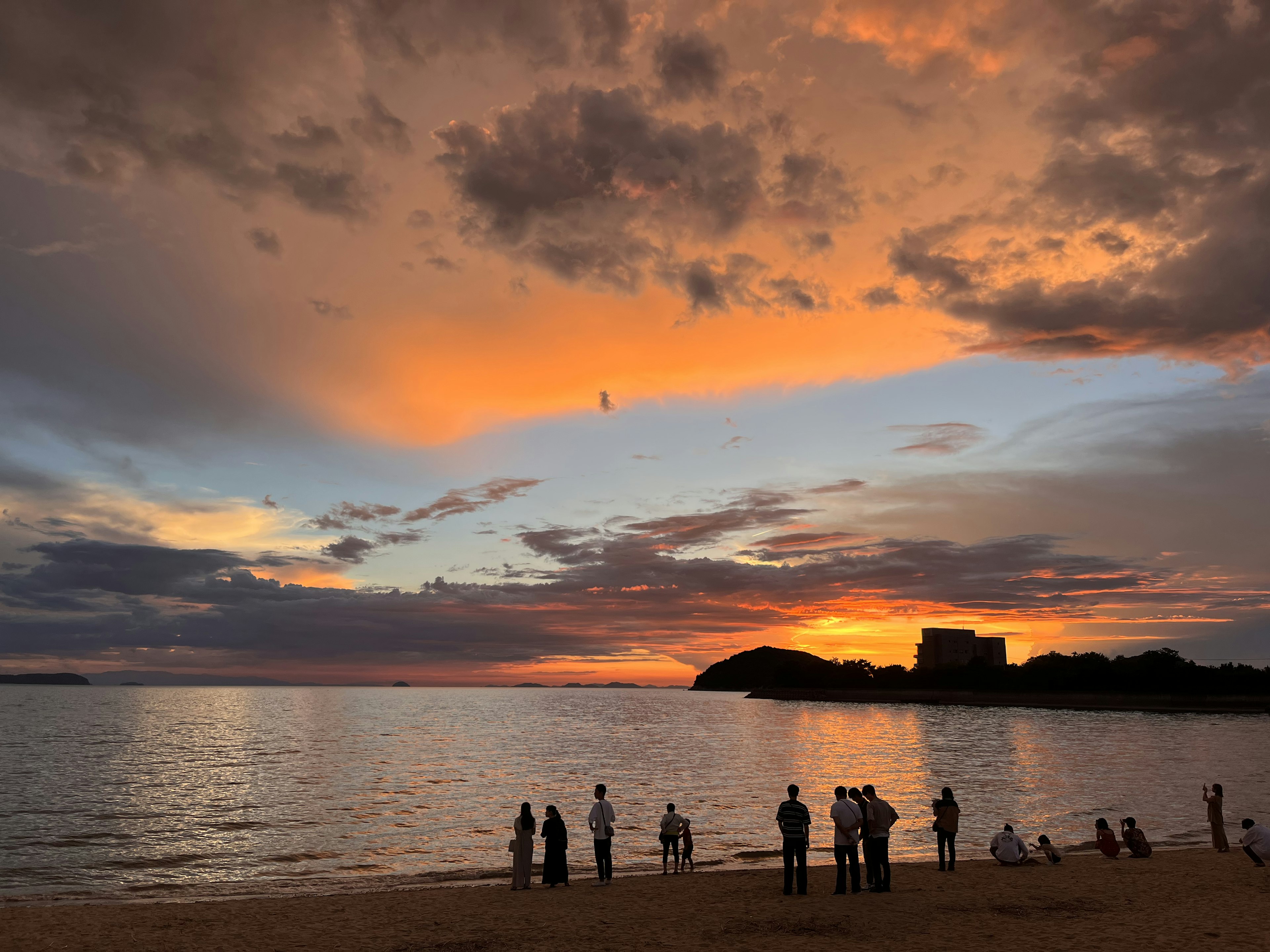 Silhouette de personnes sur la plage au coucher du soleil avec un ciel orange et bleu vif