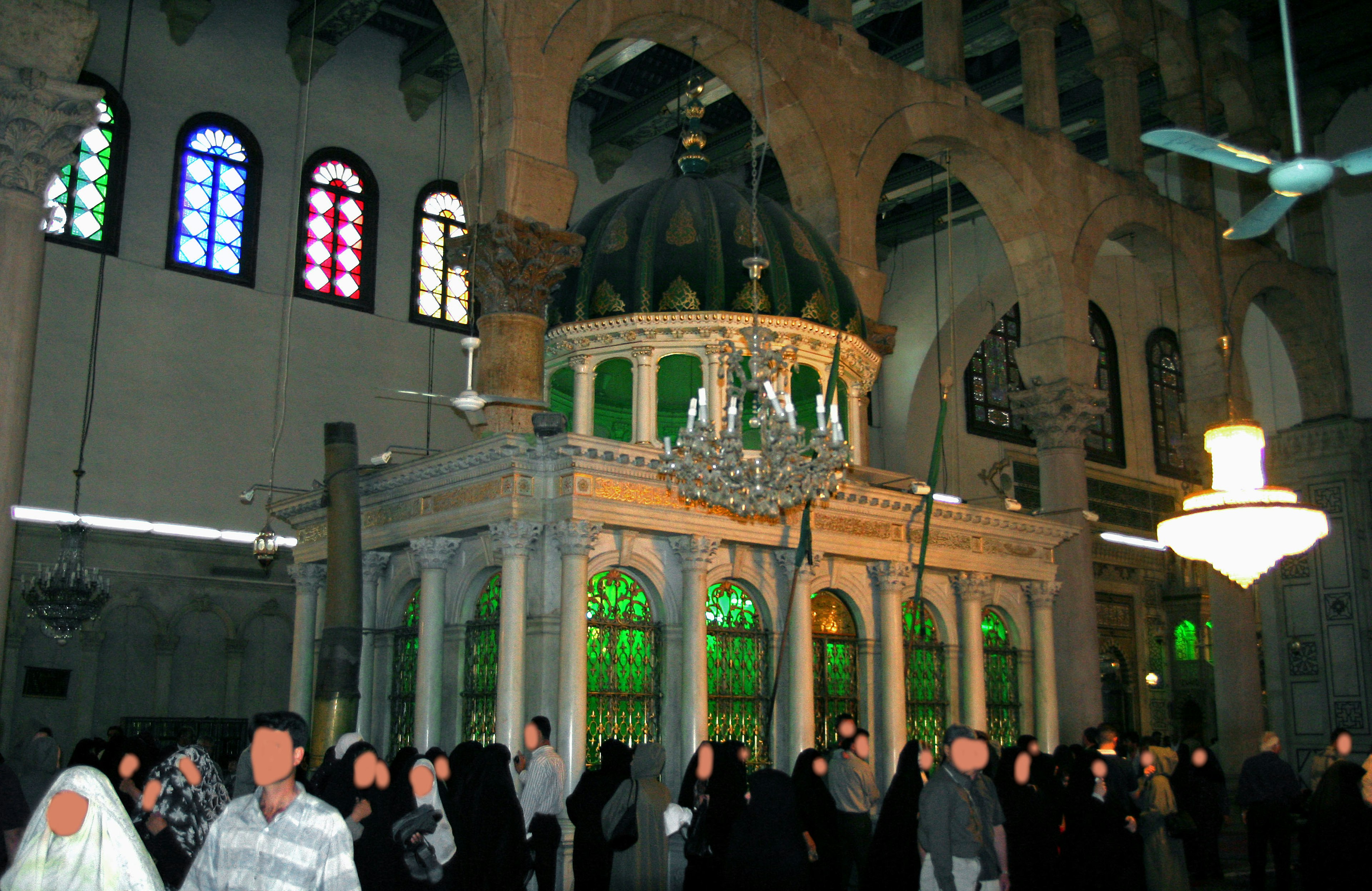 Interior de un edificio religioso con una cúpula de vidrio verde y ventanas decorativas llenas de personas