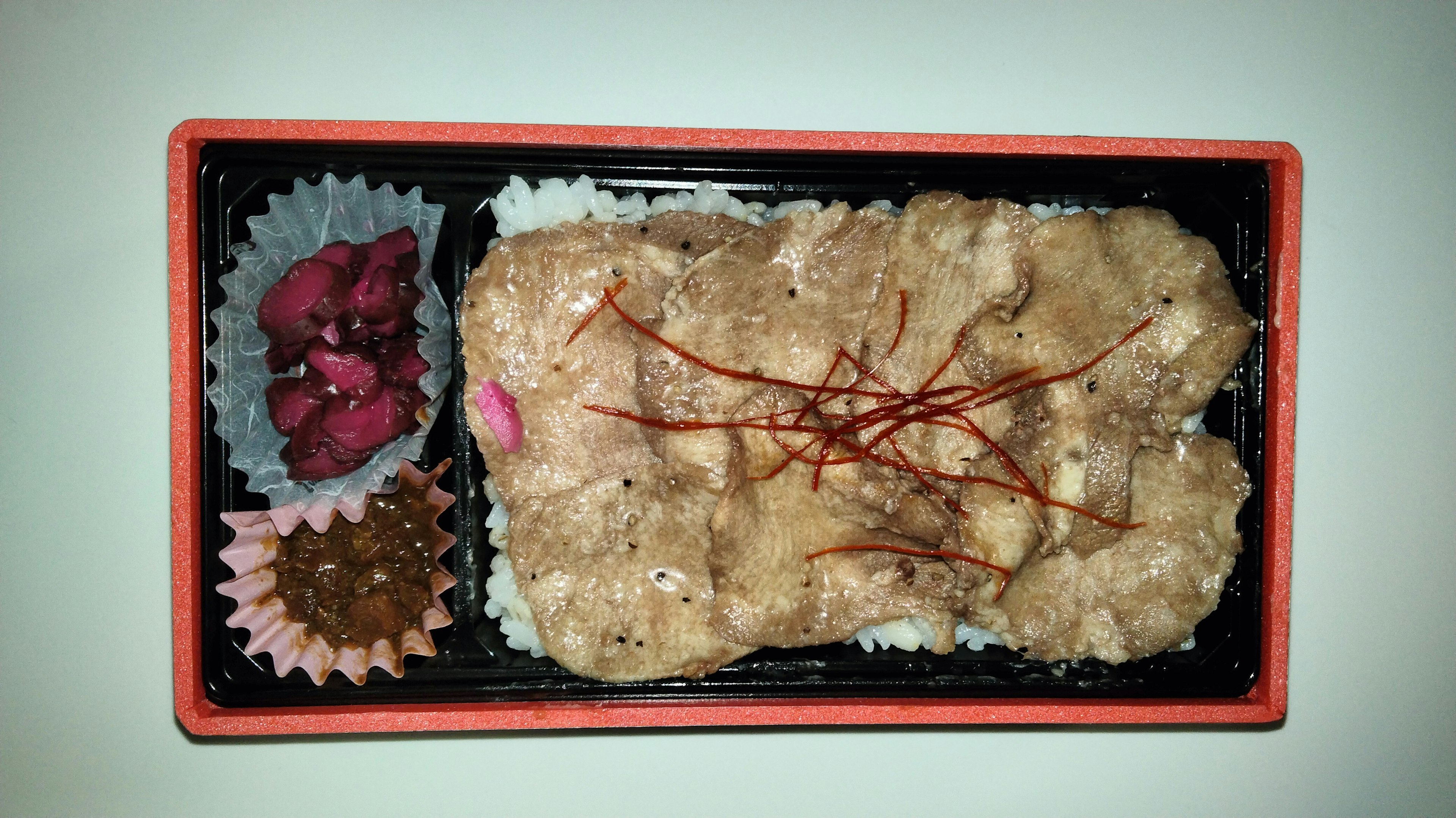 Imagen de una caja bento con pollo frito sobre arroz y guarniciones coloridas