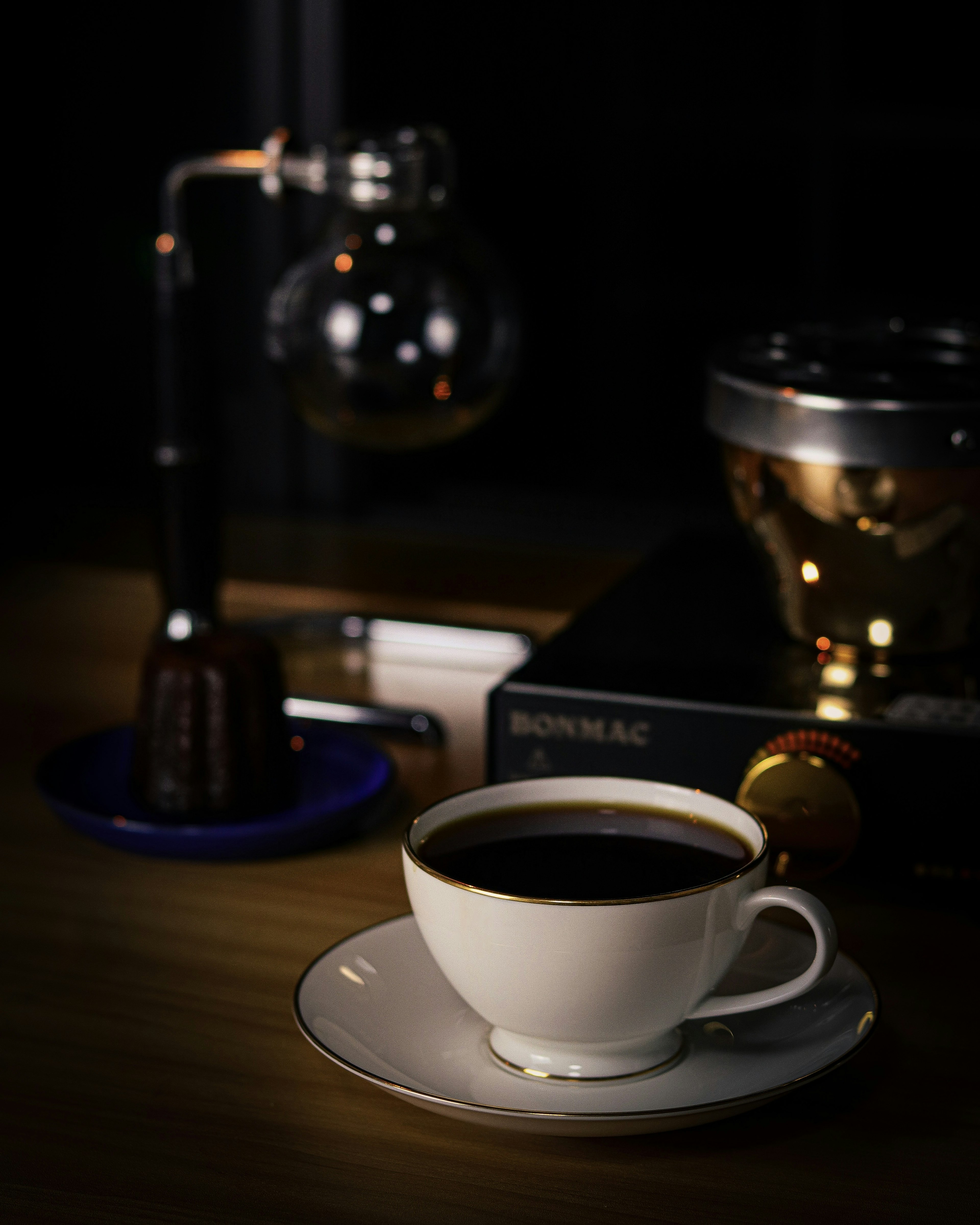 A coffee cup filled with dark coffee on a saucer near a coffee brewing device