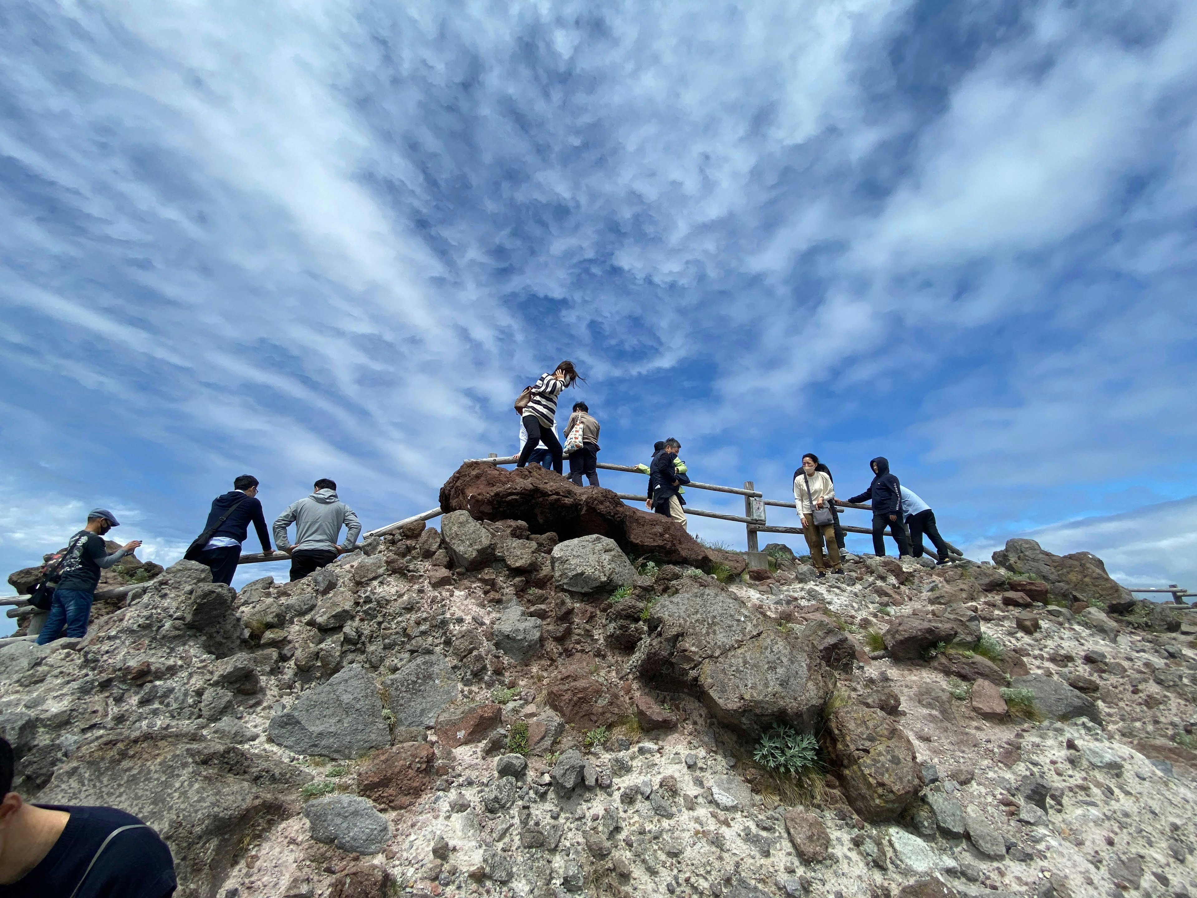 Orang-orang berdiri di puncak berbatu di bawah langit biru