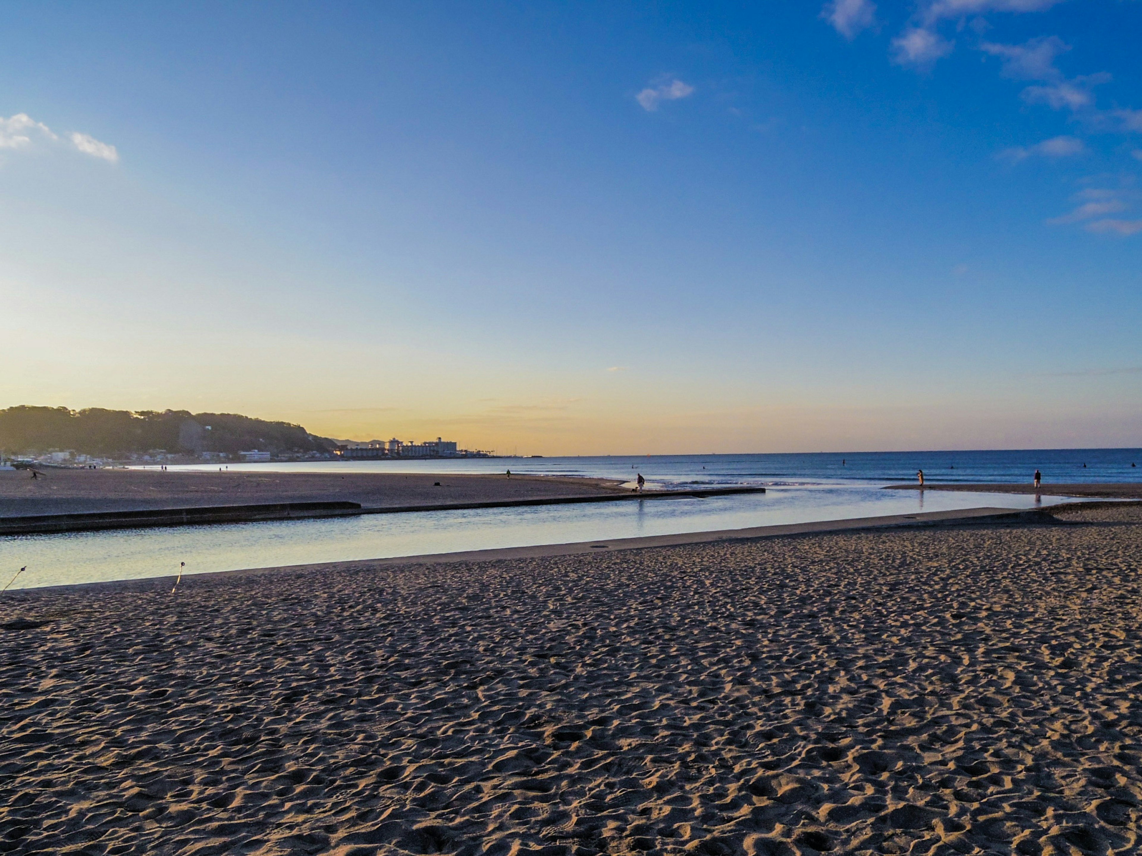 Scena di spiaggia al tramonto con acqua calma e persone che passeggiano