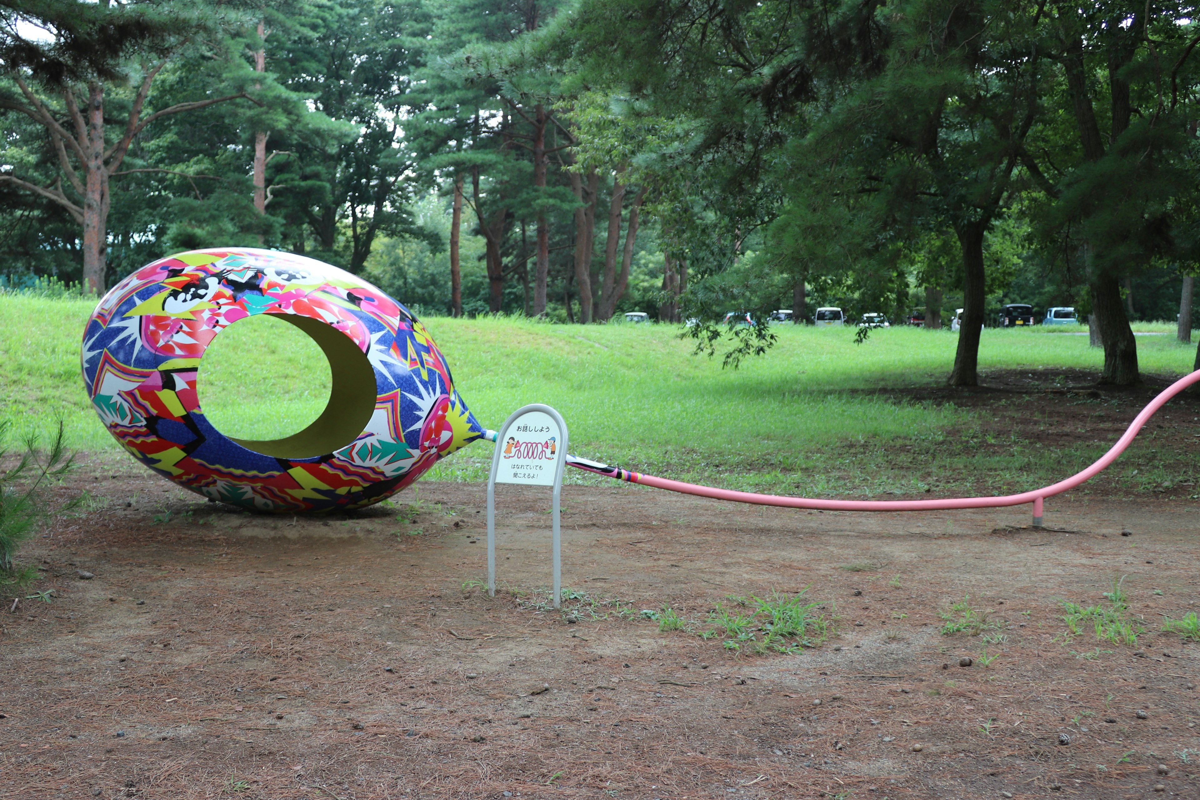 Instalación artística en forma de huevo colorido con una manguera larga sobre un terreno de hierba