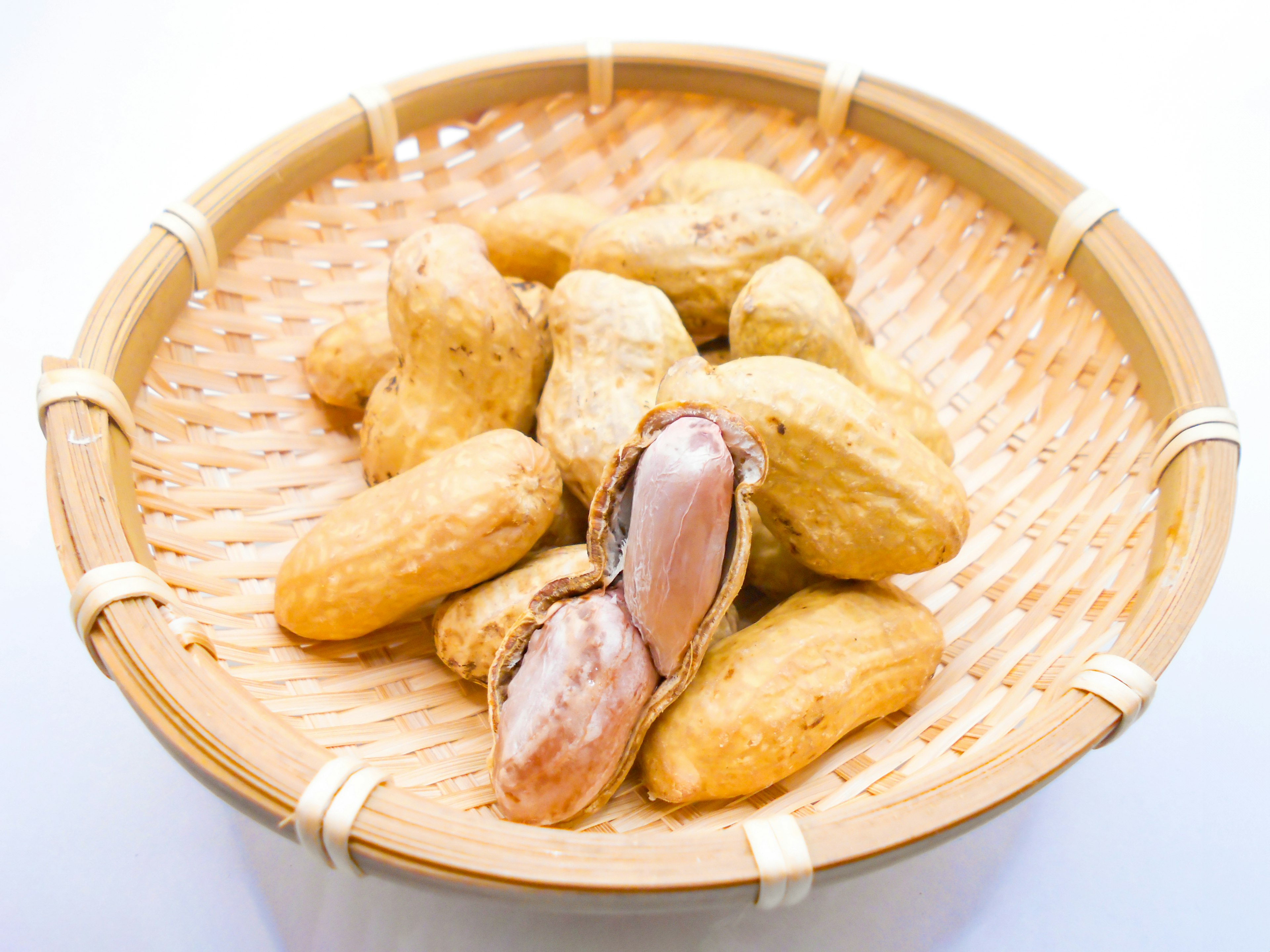 A photo of peanuts in a wicker basket some peanuts are cracked revealing the inside