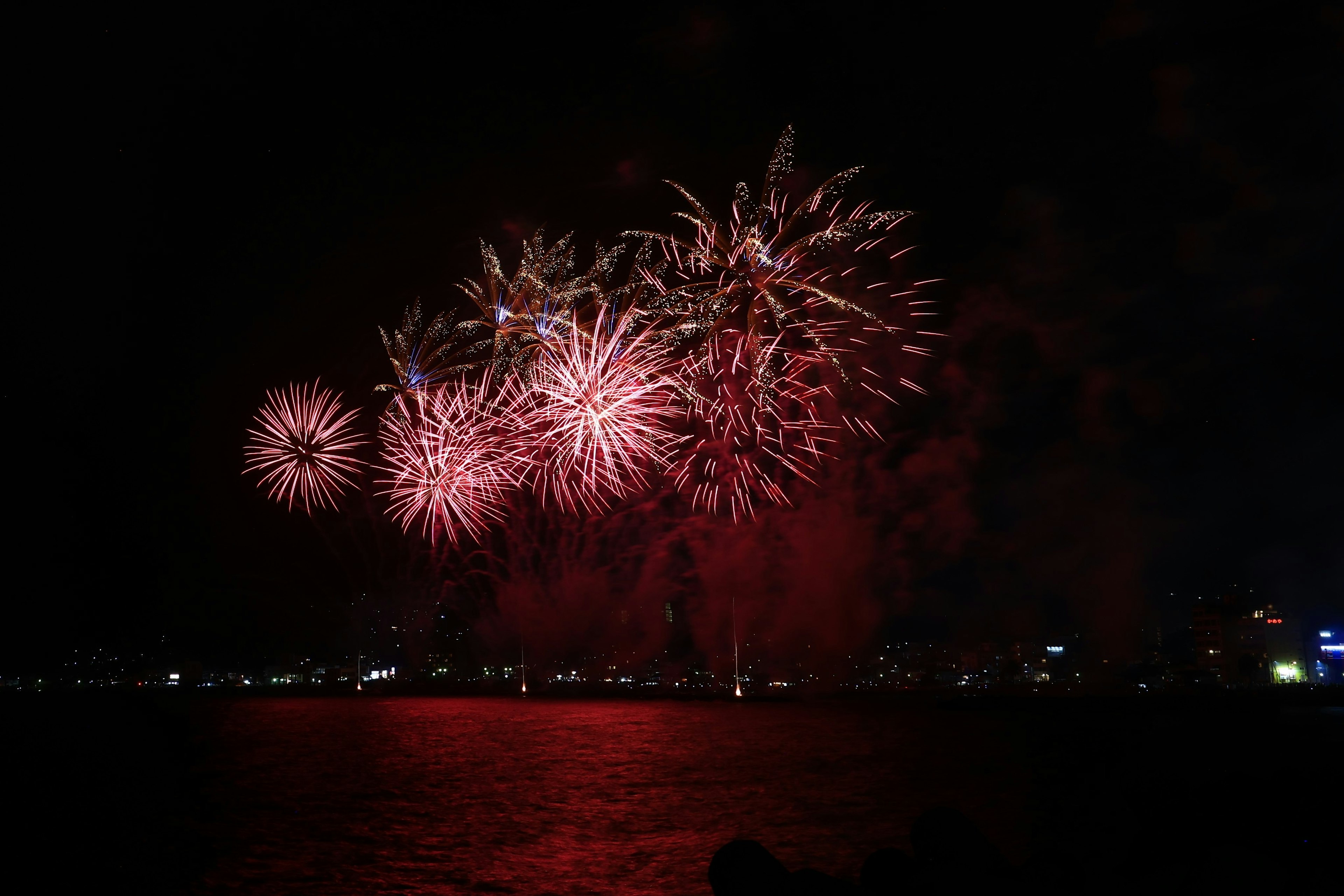 Red fireworks illuminating the night sky and reflecting on the water