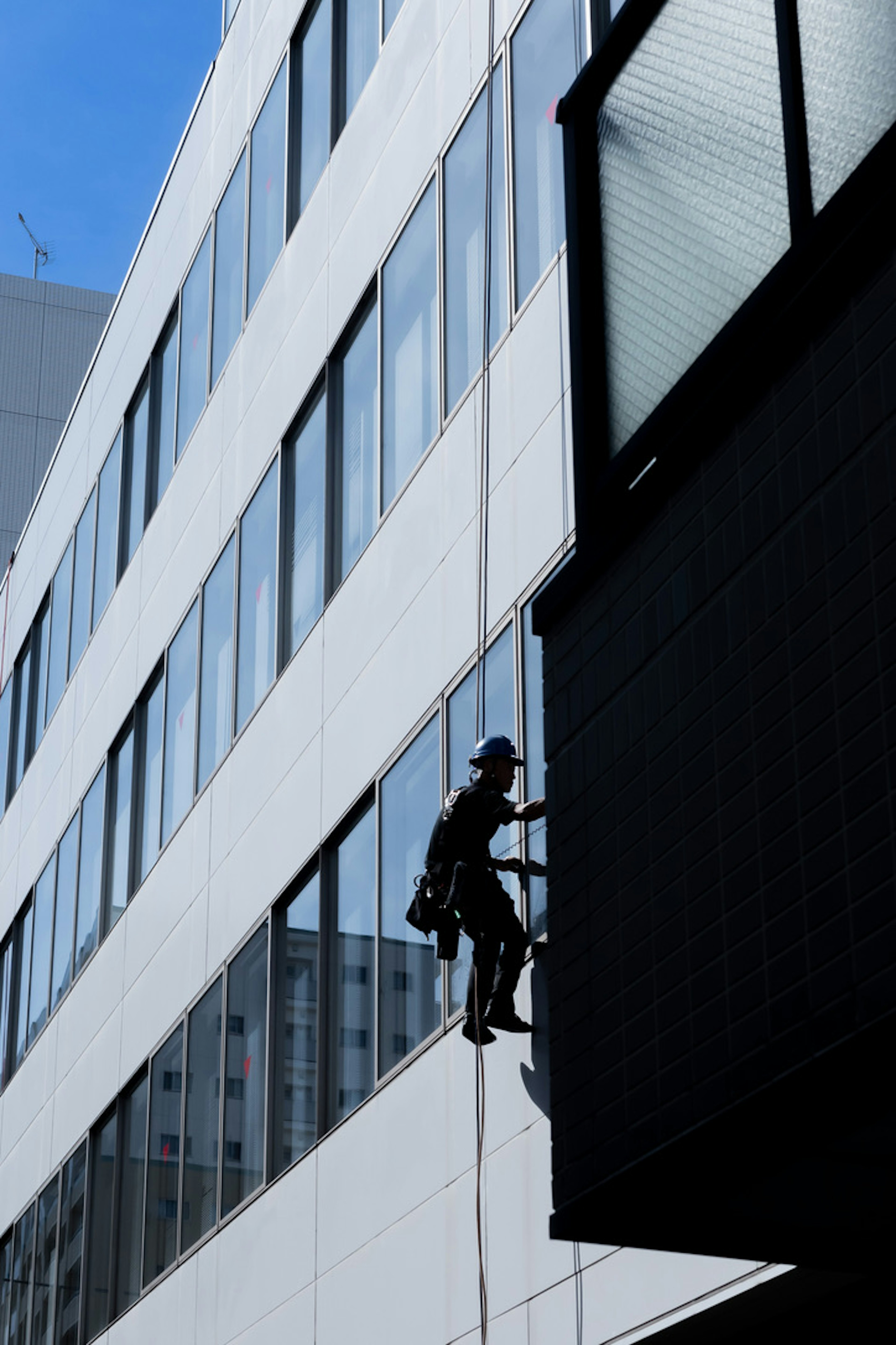 Silhouette eines Arbeiters, der Fenster an einem Gebäude reinigt