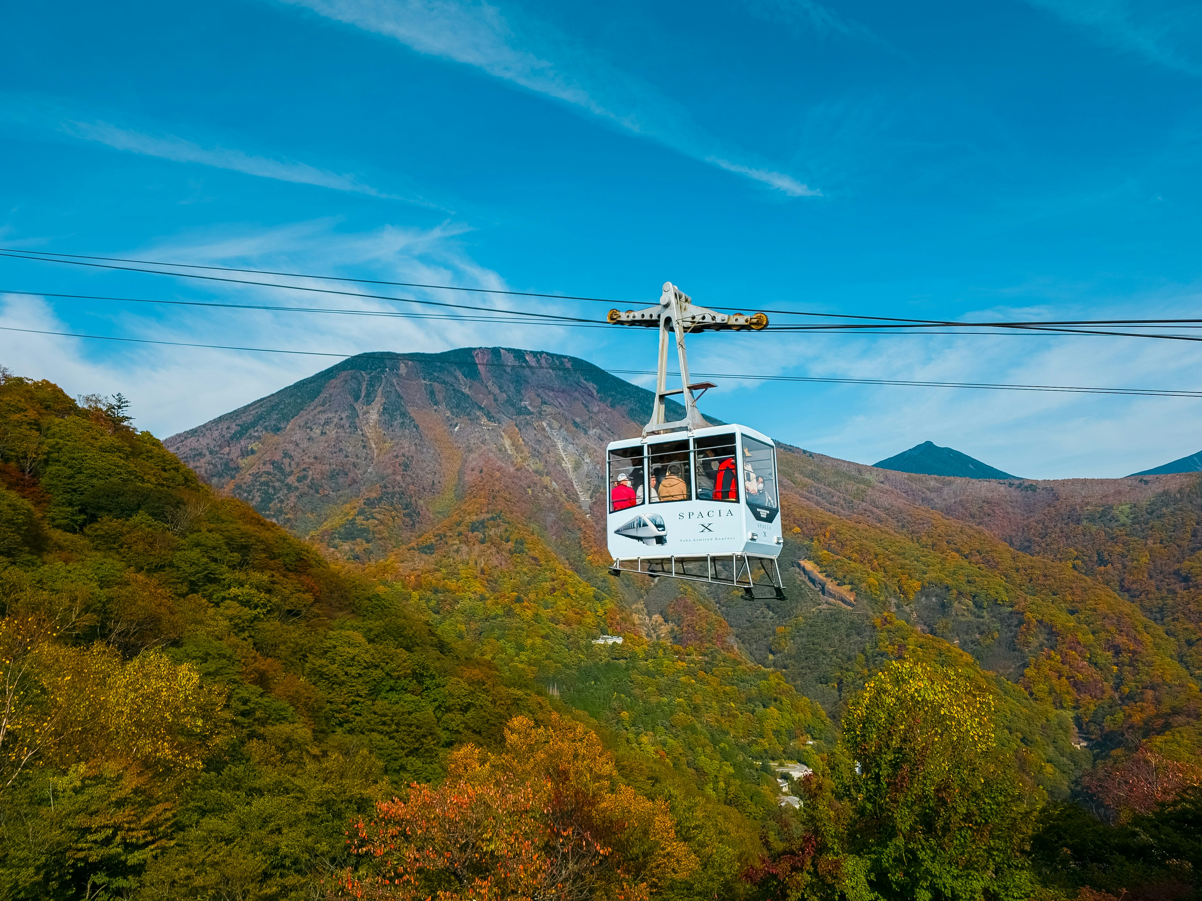 A gondola moving through colorful autumn mountains under a blue sky