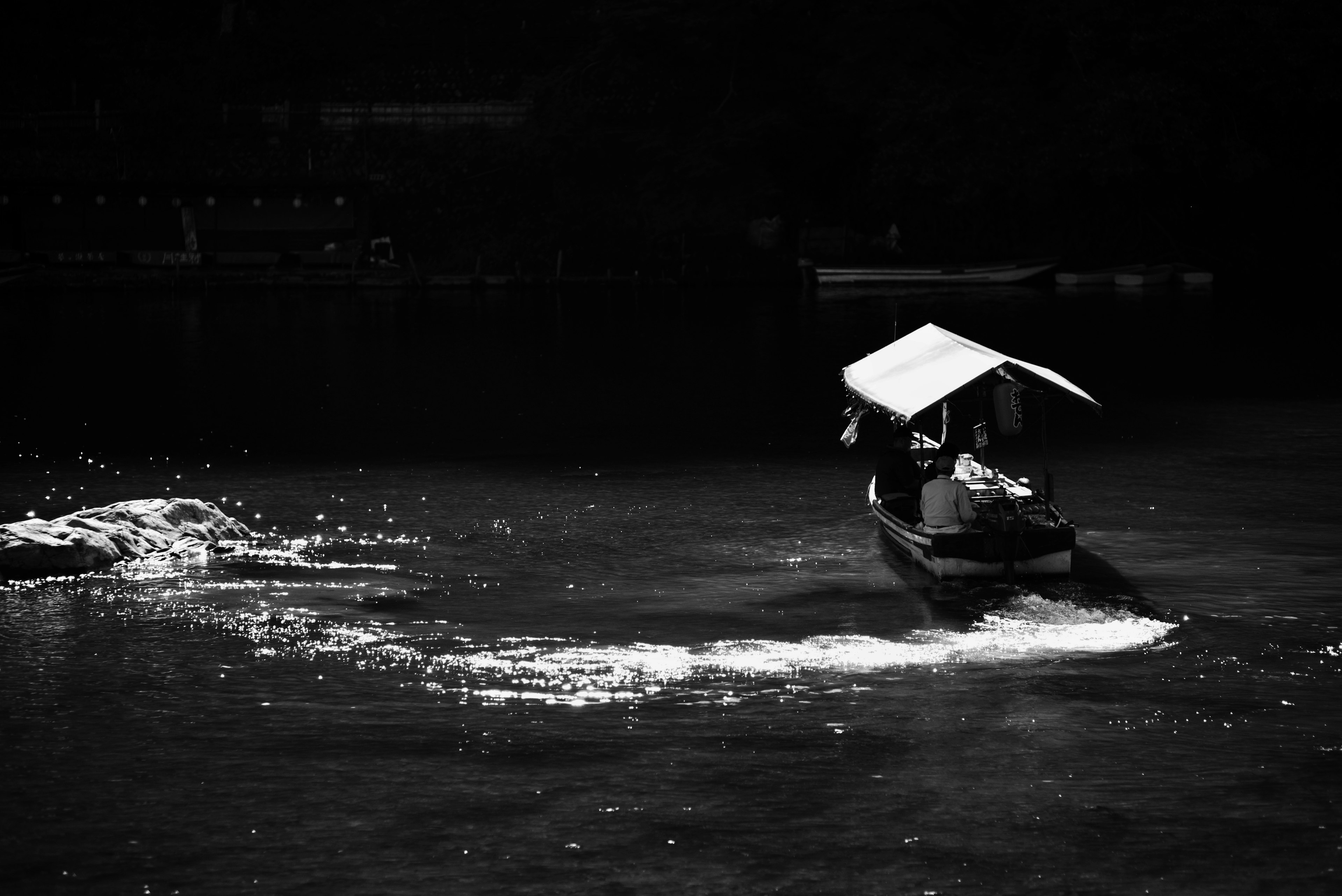 A small boat moving across a black and white water surface with trailing waves