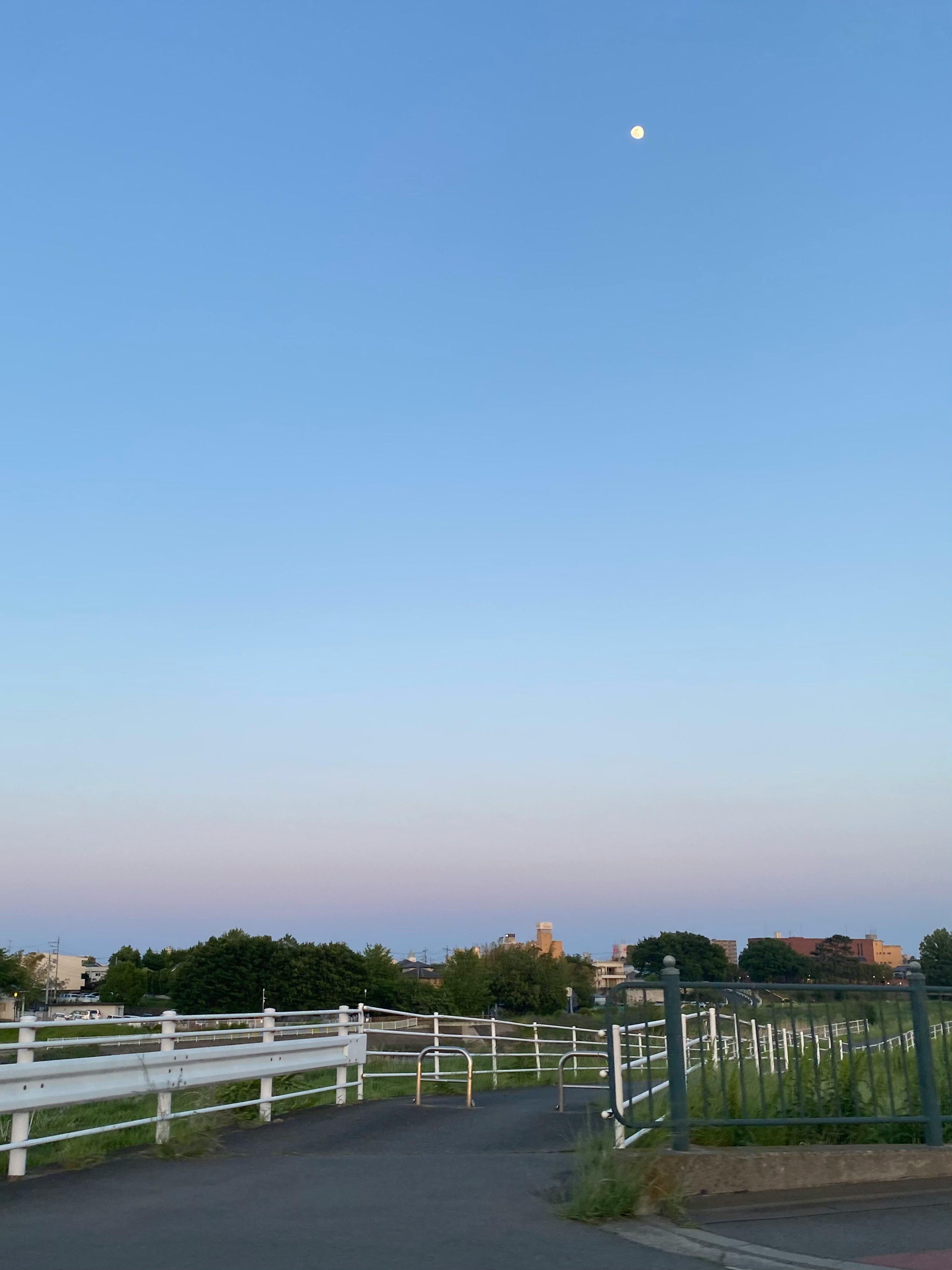 青い空と白いフェンスのある田舎道の風景　月が空に浮かんでいる