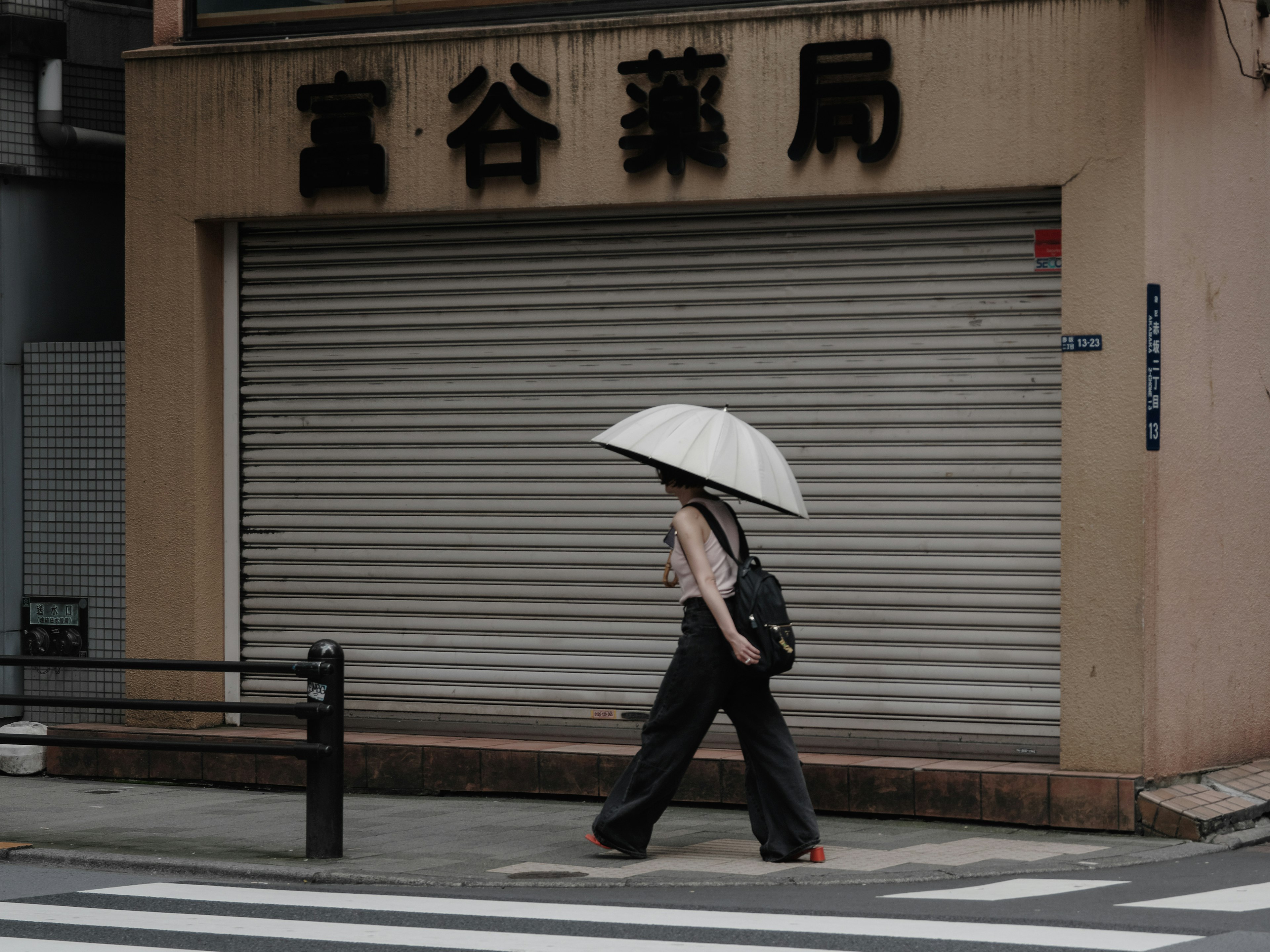 A woman walking with a white umbrella in front of a closed pharmacy with a shutter