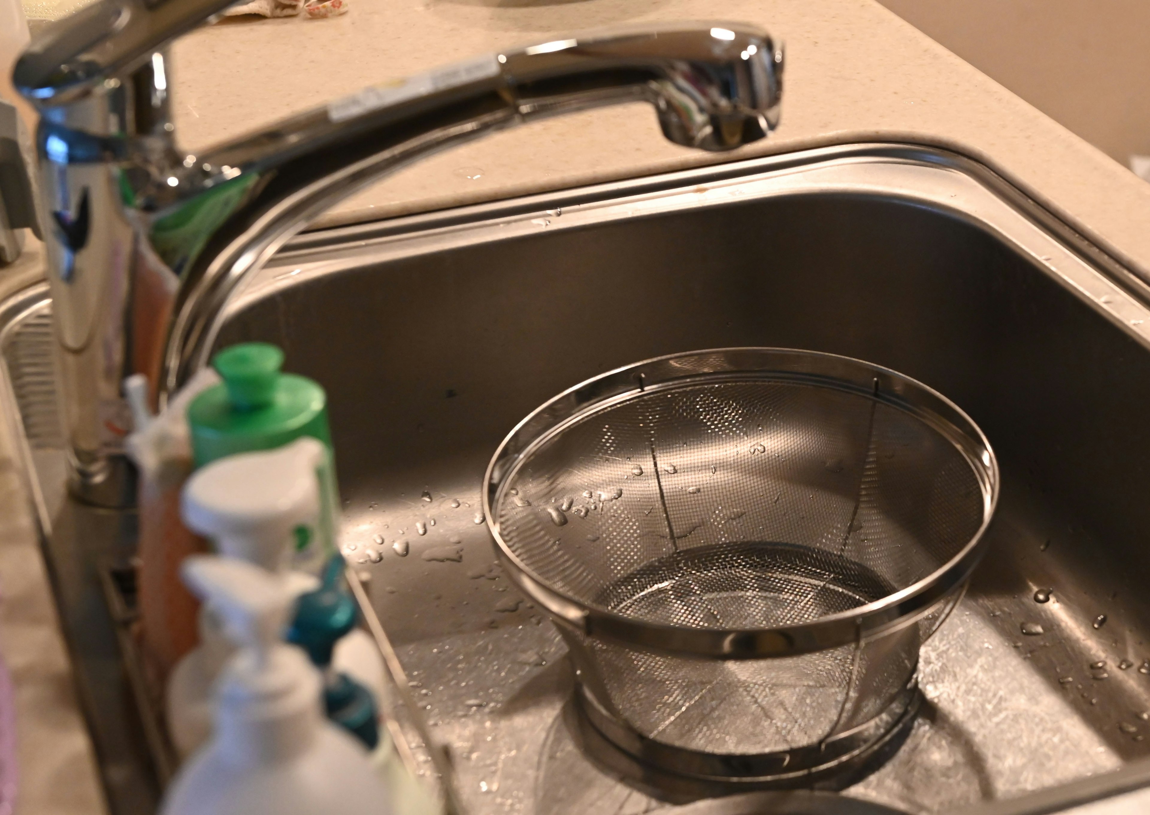 A metal bowl in a kitchen sink with various bottles of dish soap nearby