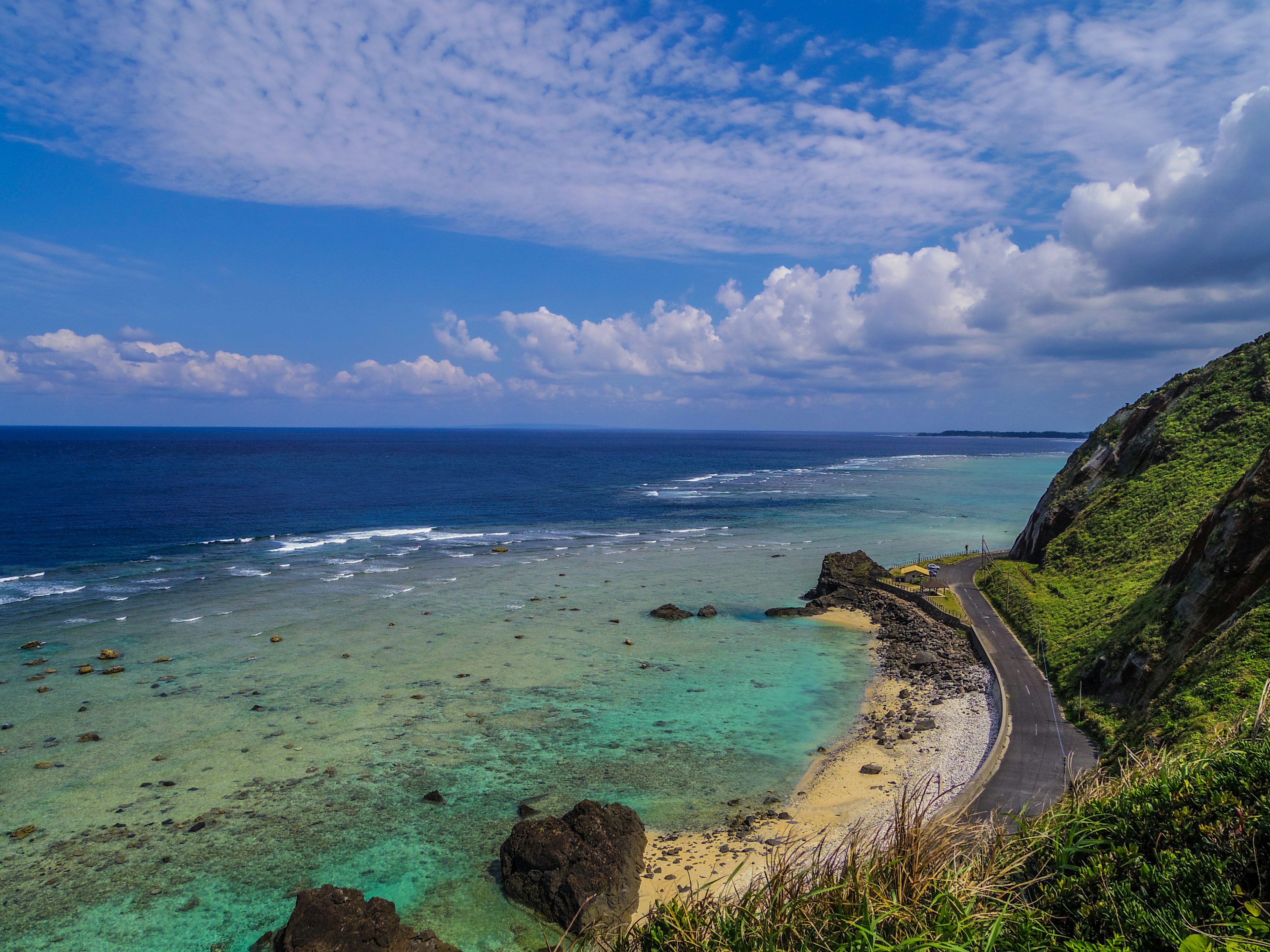 Kurvenreiche Straße entlang einer Küste mit blauem Meer und grünen Hügeln