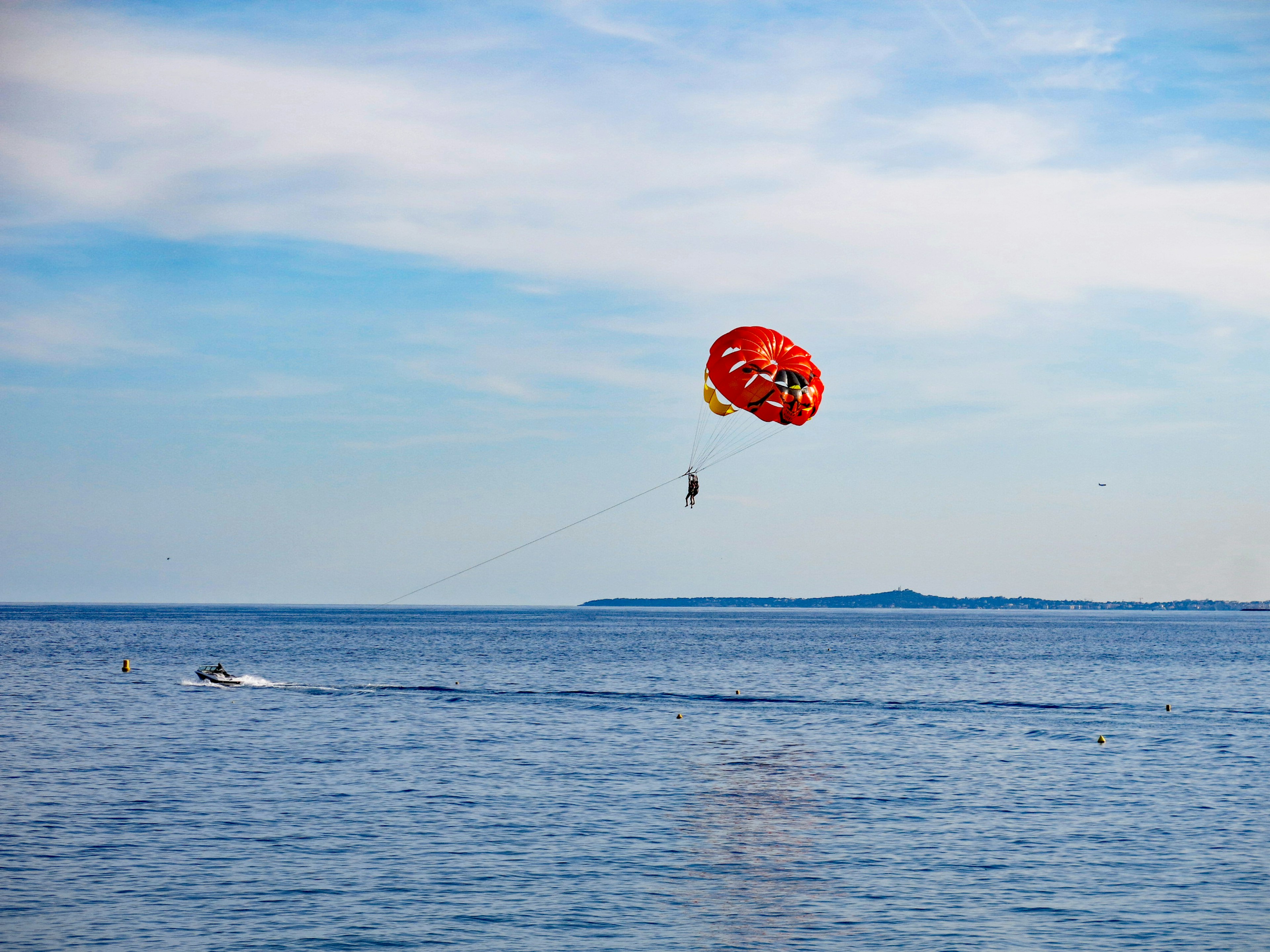 青い海の上空に赤いパラシュートが広がり、パラセーリングを楽しむ人が見える