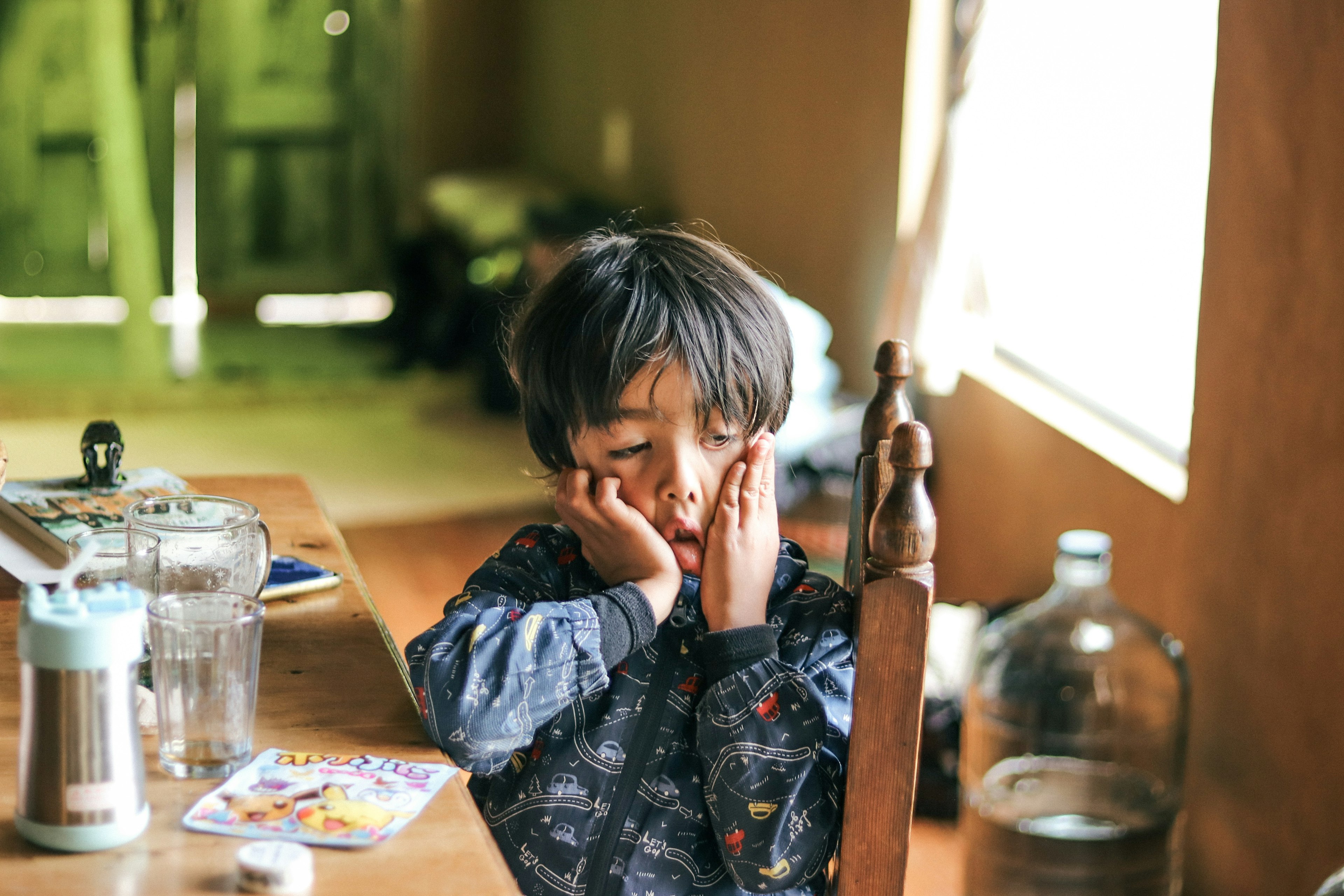 一個疲倦的孩子坐在桌子前雙手托腮周圍有瓶子和雜誌