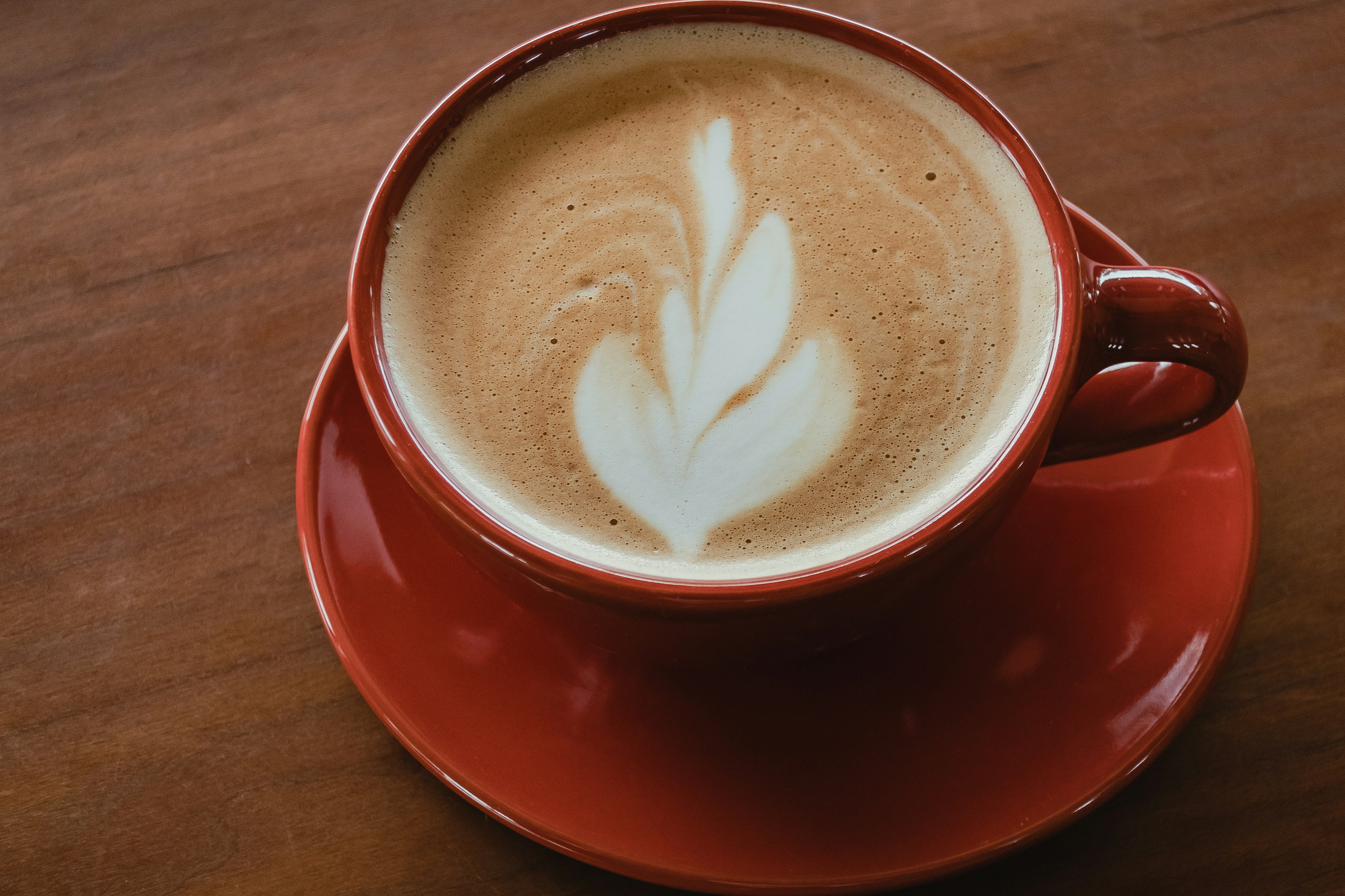 Café dans une tasse rouge avec un motif de latte art en forme de feuille