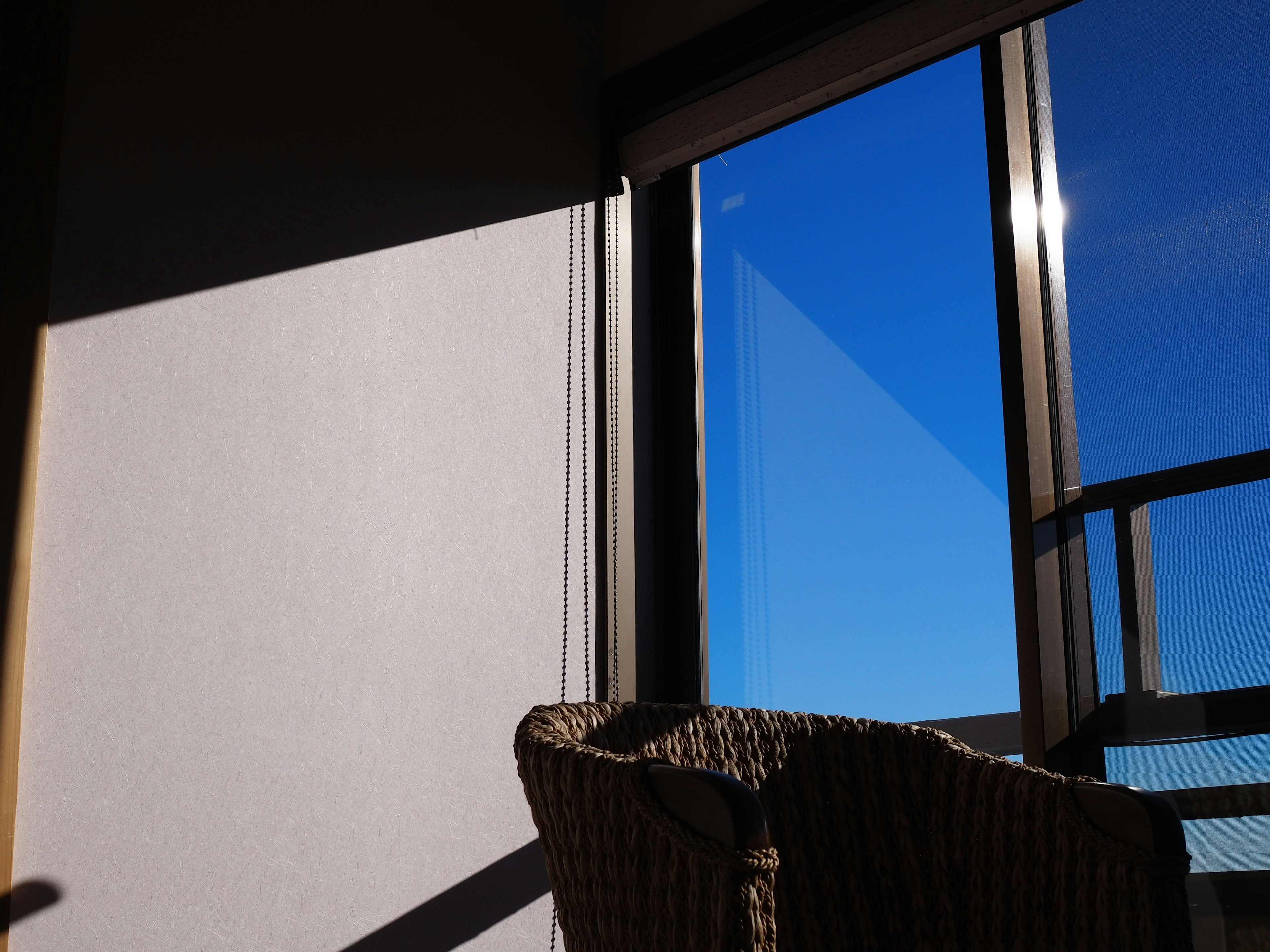 Schatten eines Stuhls neben einem Fenster mit einem hellblauen Himmel