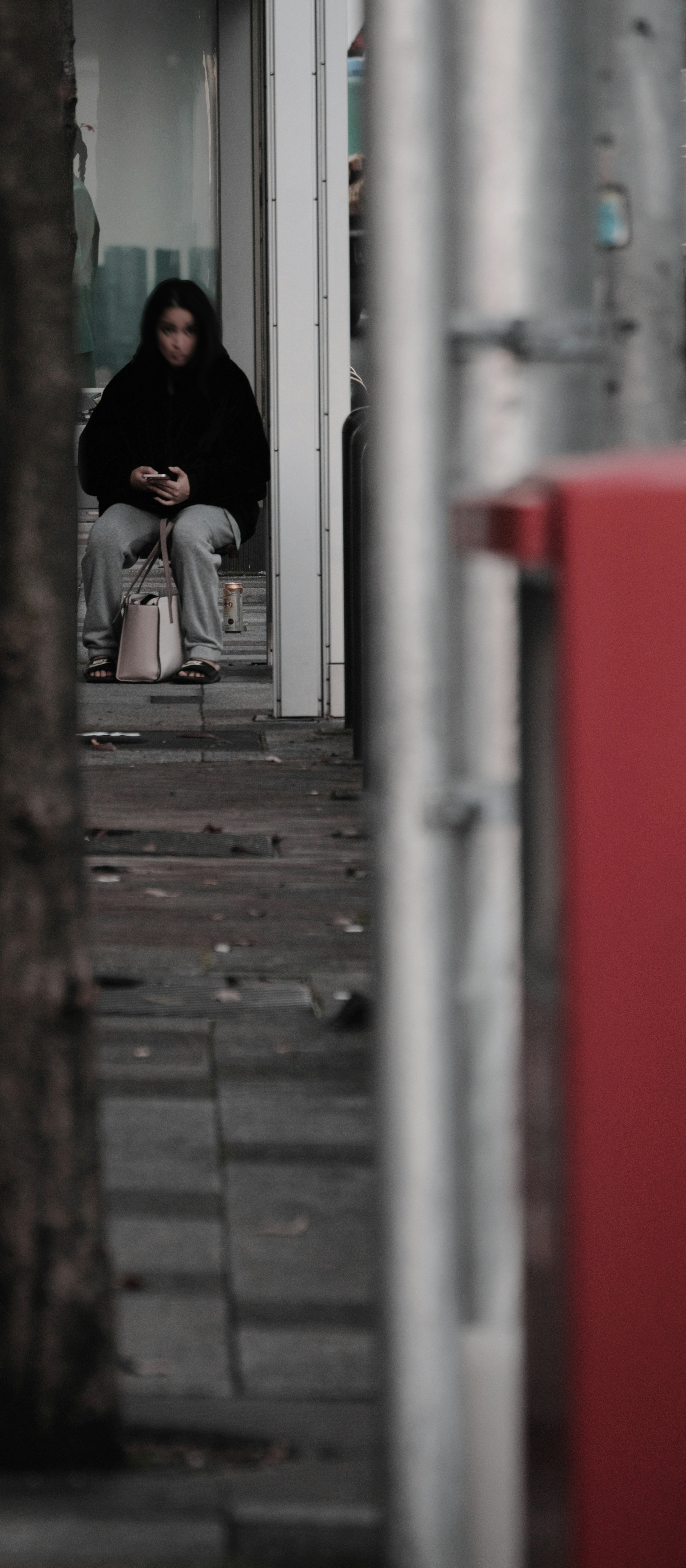 A woman sitting on a street wearing dark clothing and holding a smartphone