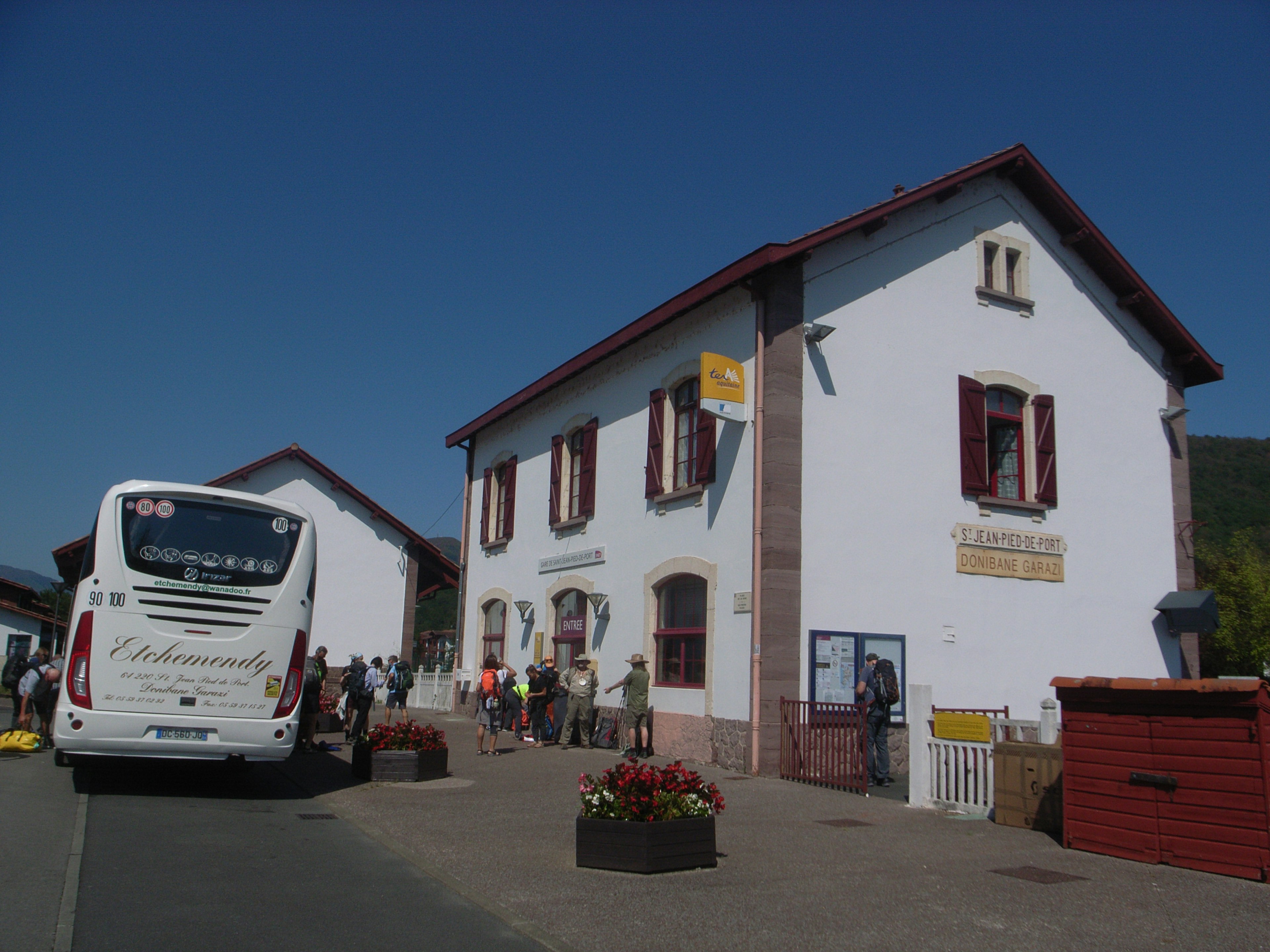 Weißes Bahnhofsgebäude mit roten Fenstern mit einem Bus und Menschen