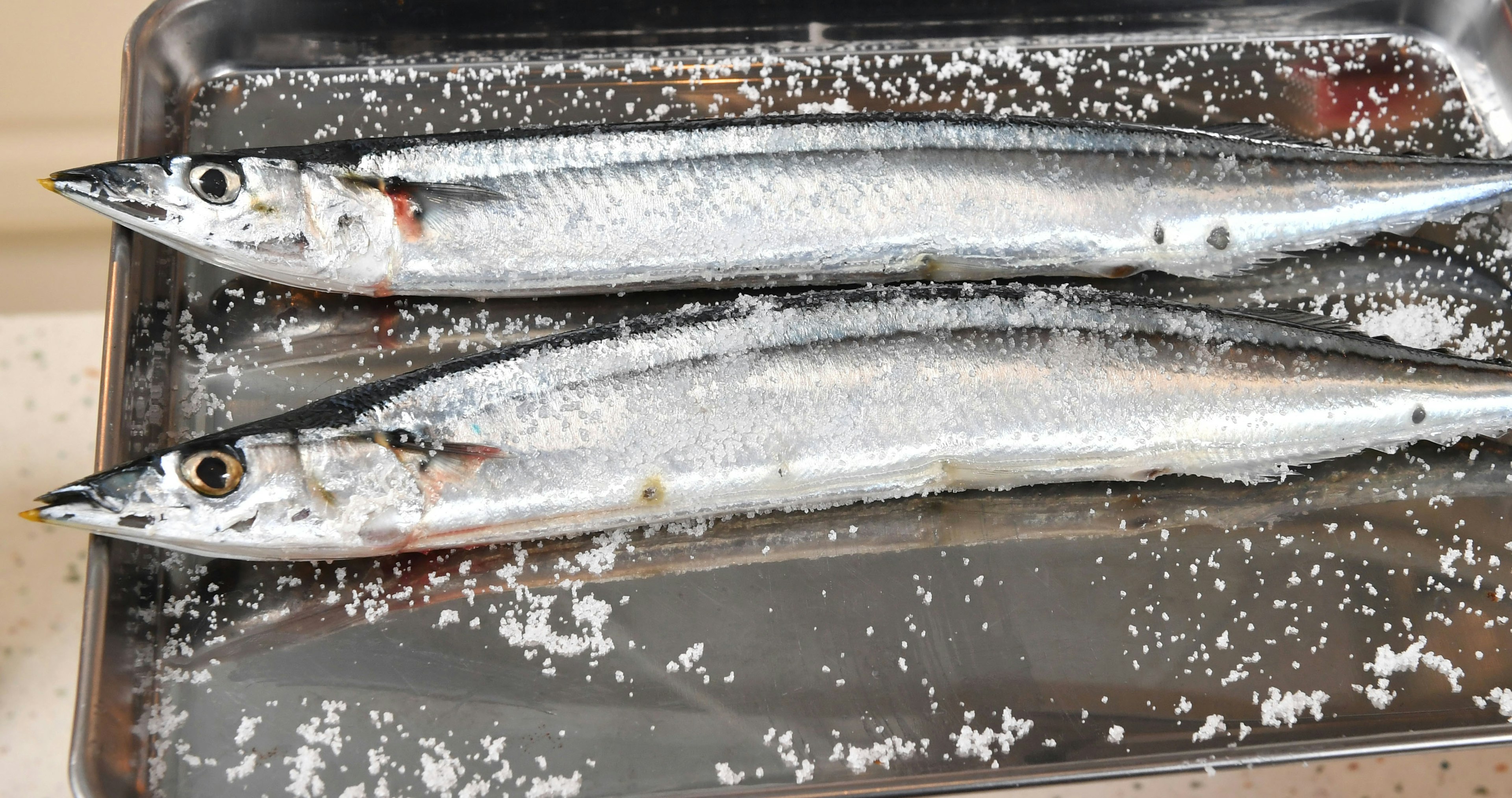 Two silver fish laid out on a tray with salt sprinkled over them