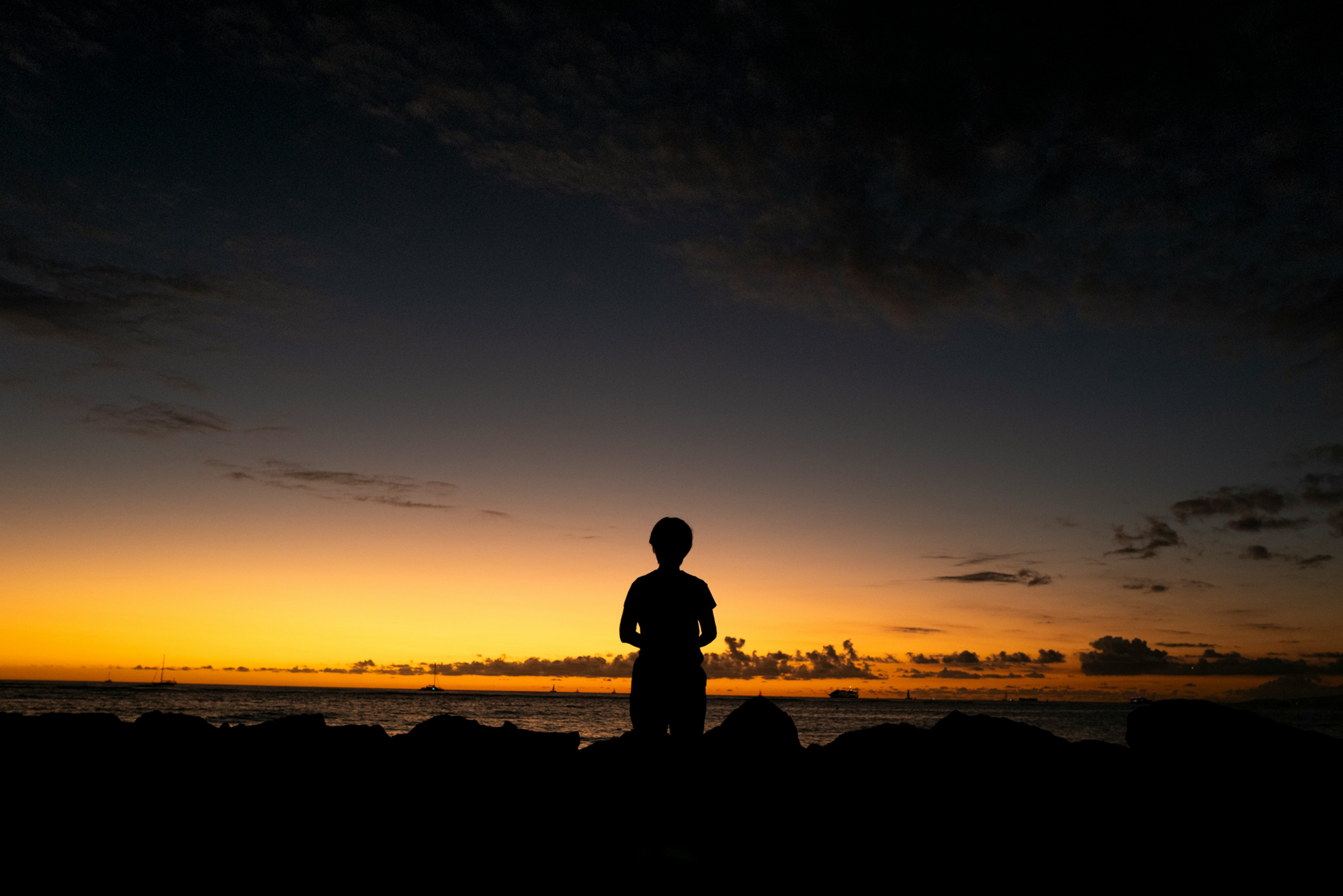 Silhouette einer Person, die am Strand bei Sonnenuntergang steht, mit lebhaftem orange-blauem Farbverlauf