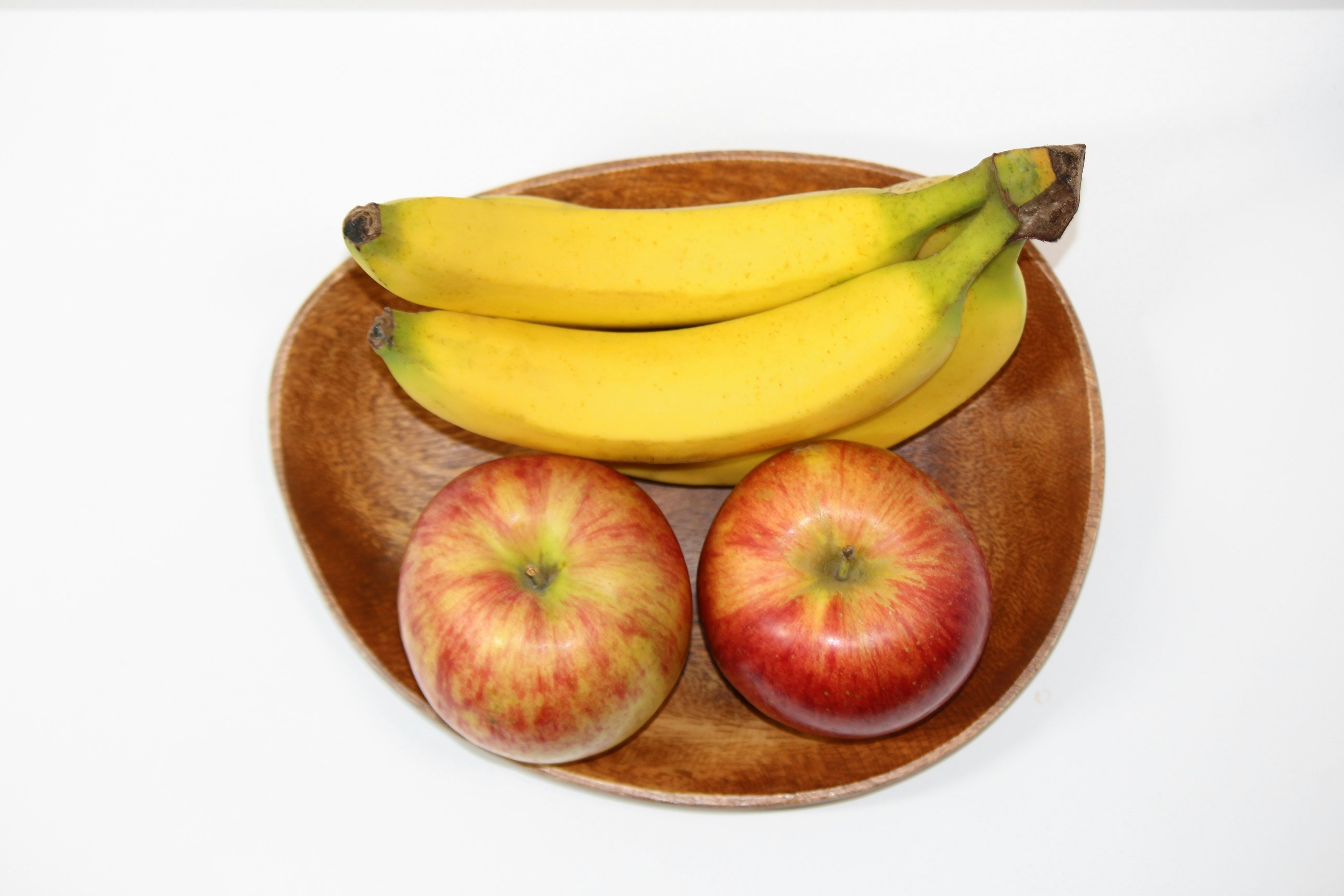 A wooden plate with a bunch of bananas and two apples