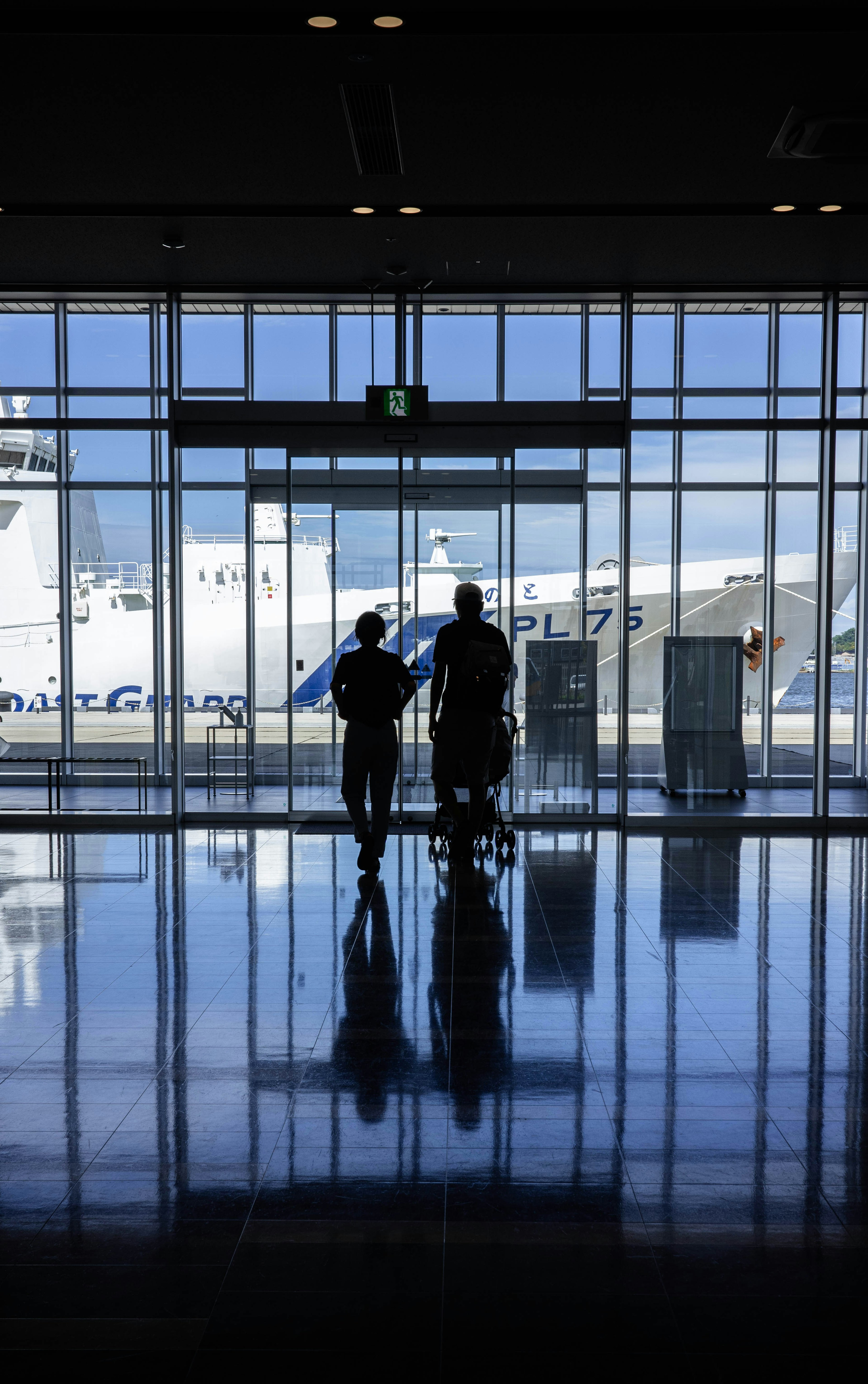 Silhouettes of two people standing in front of large glass windows at an airport