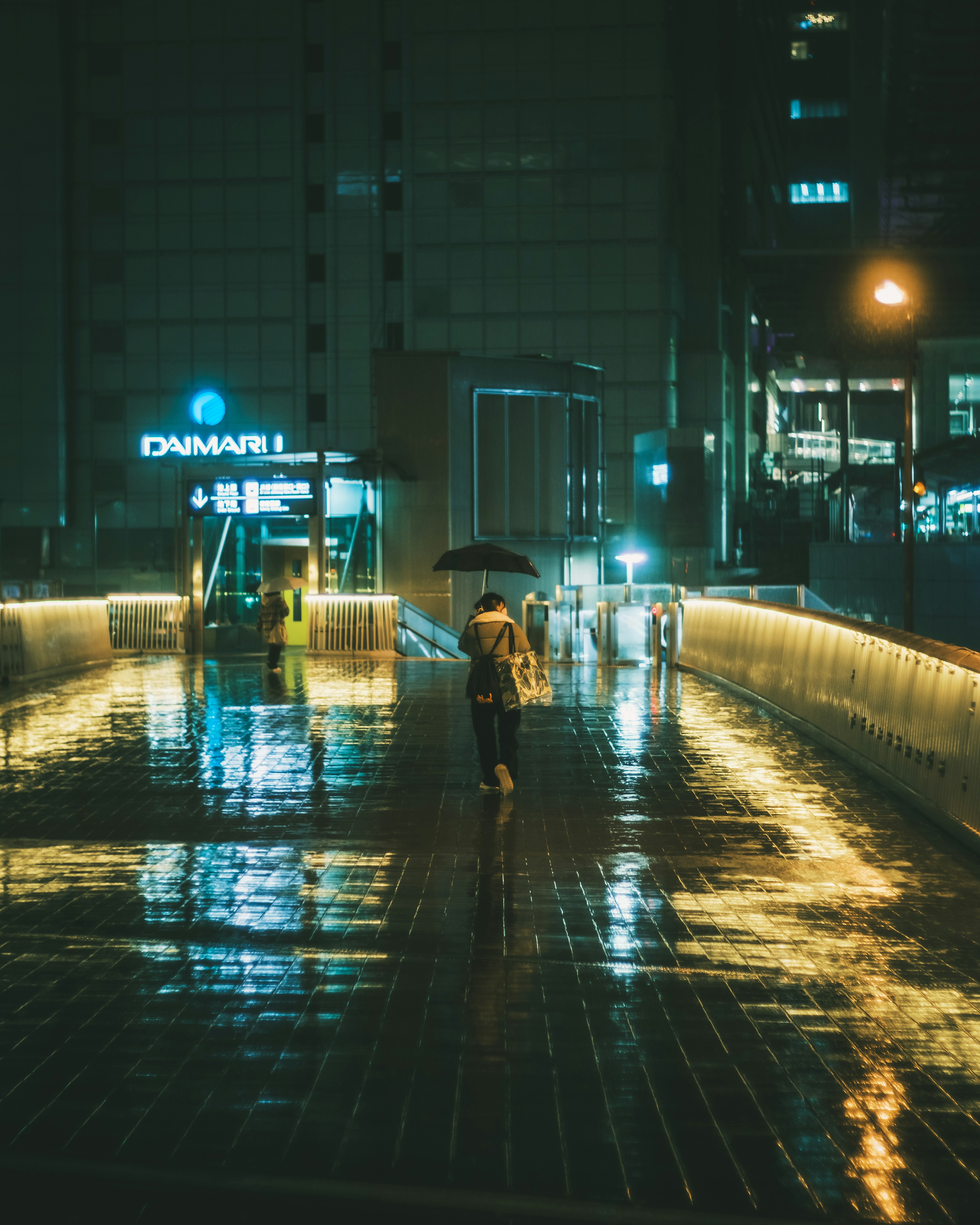 A person walking with an umbrella on a rainy night reflecting lights on the pavement