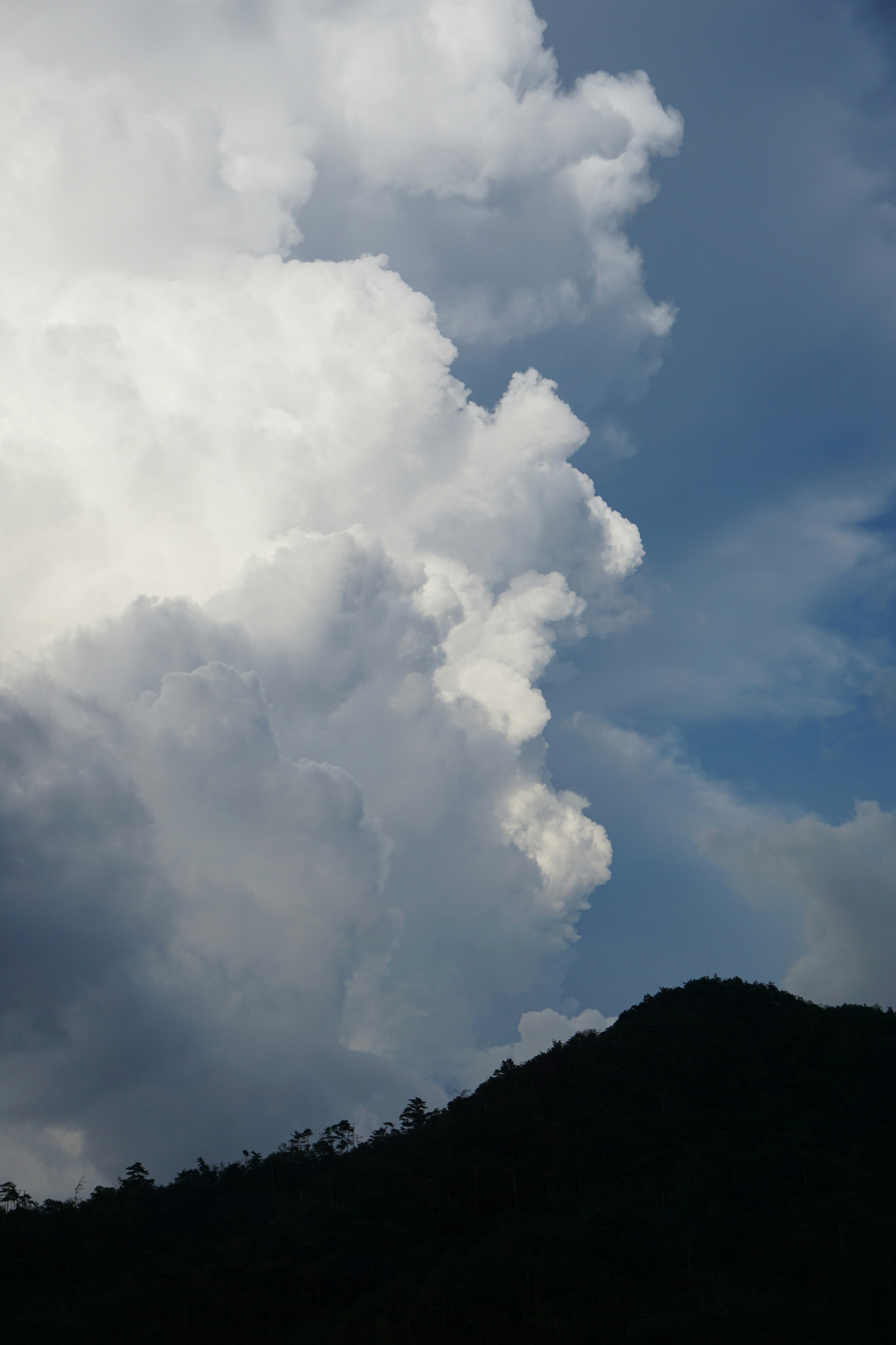 Un paysage avec des nuages blancs contre un ciel bleu et une silhouette de montagne