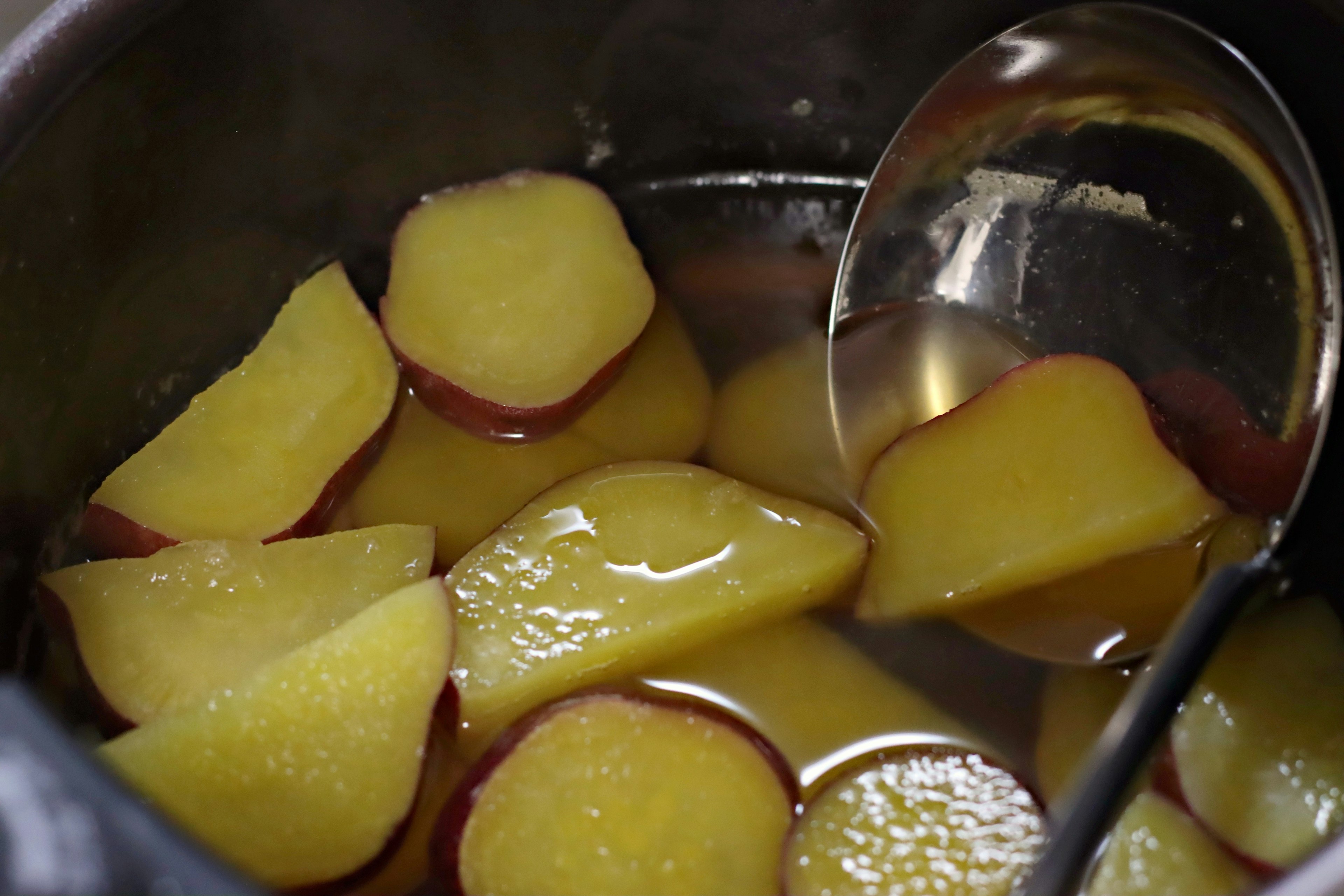 Sliced sweet potatoes submerged in syrup inside a pot