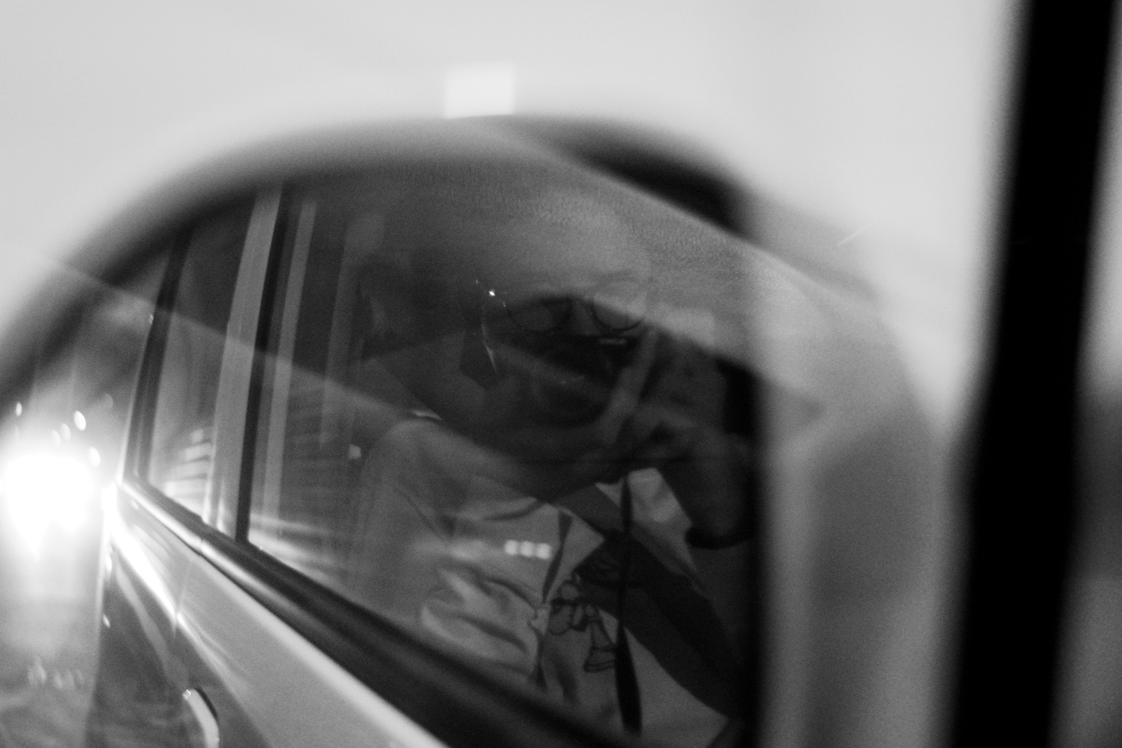 Réflexion en noir et blanc d'un paysage et d'un conducteur dans un rétroviseur de voiture