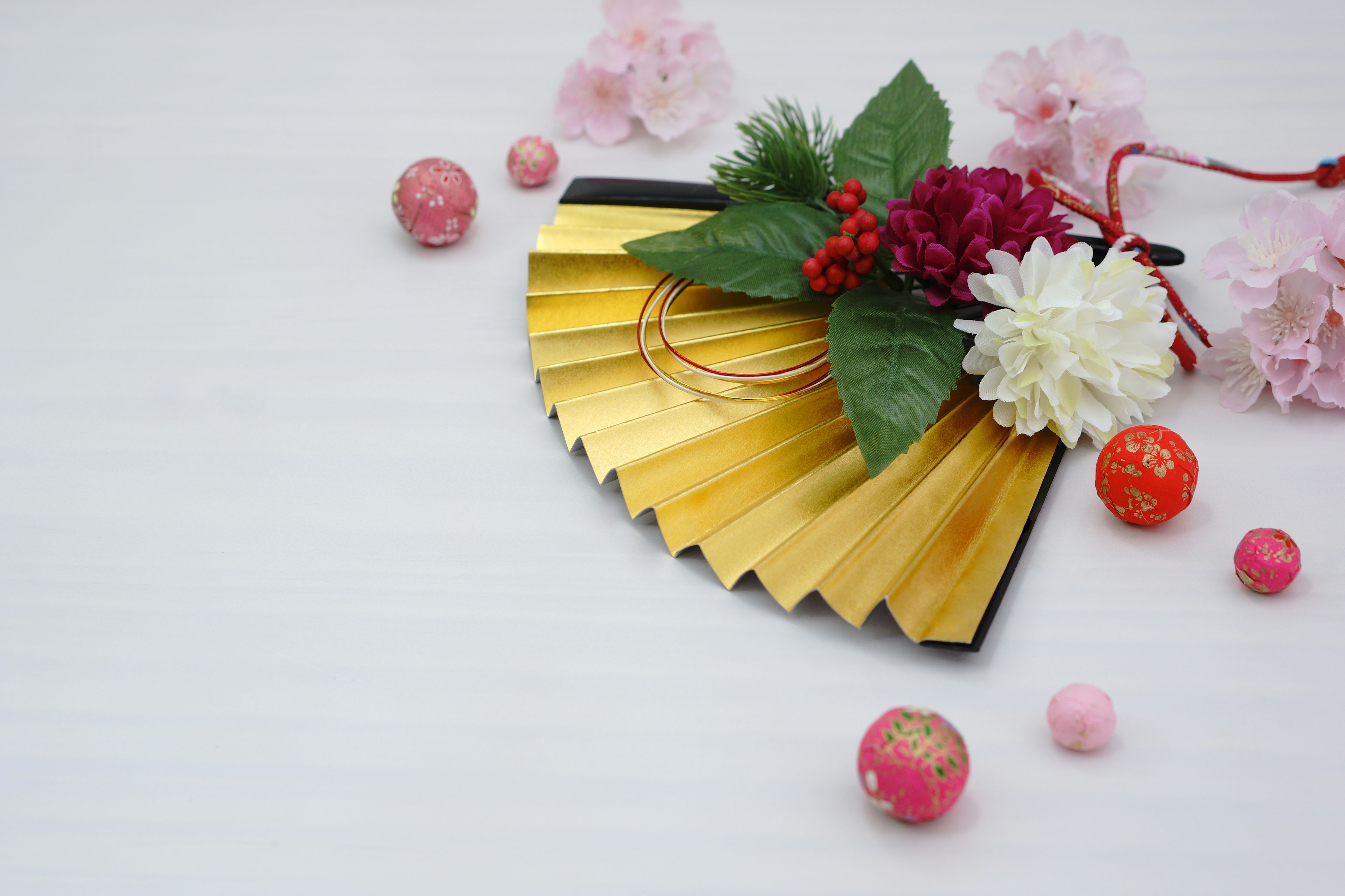 A golden fan with floral arrangement and decorative balls on a light background