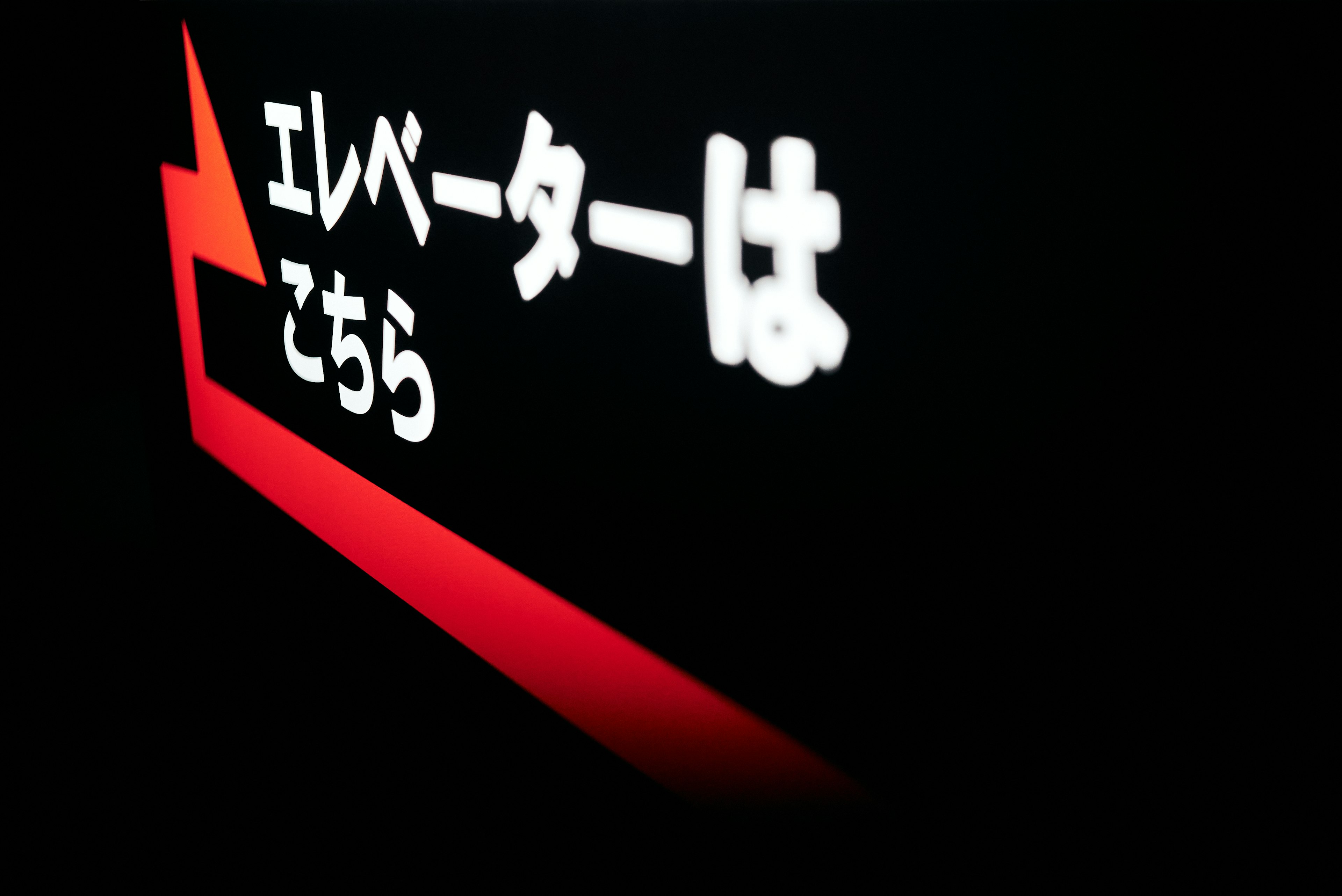 Elevator direction sign with red arrow and white text on dark background