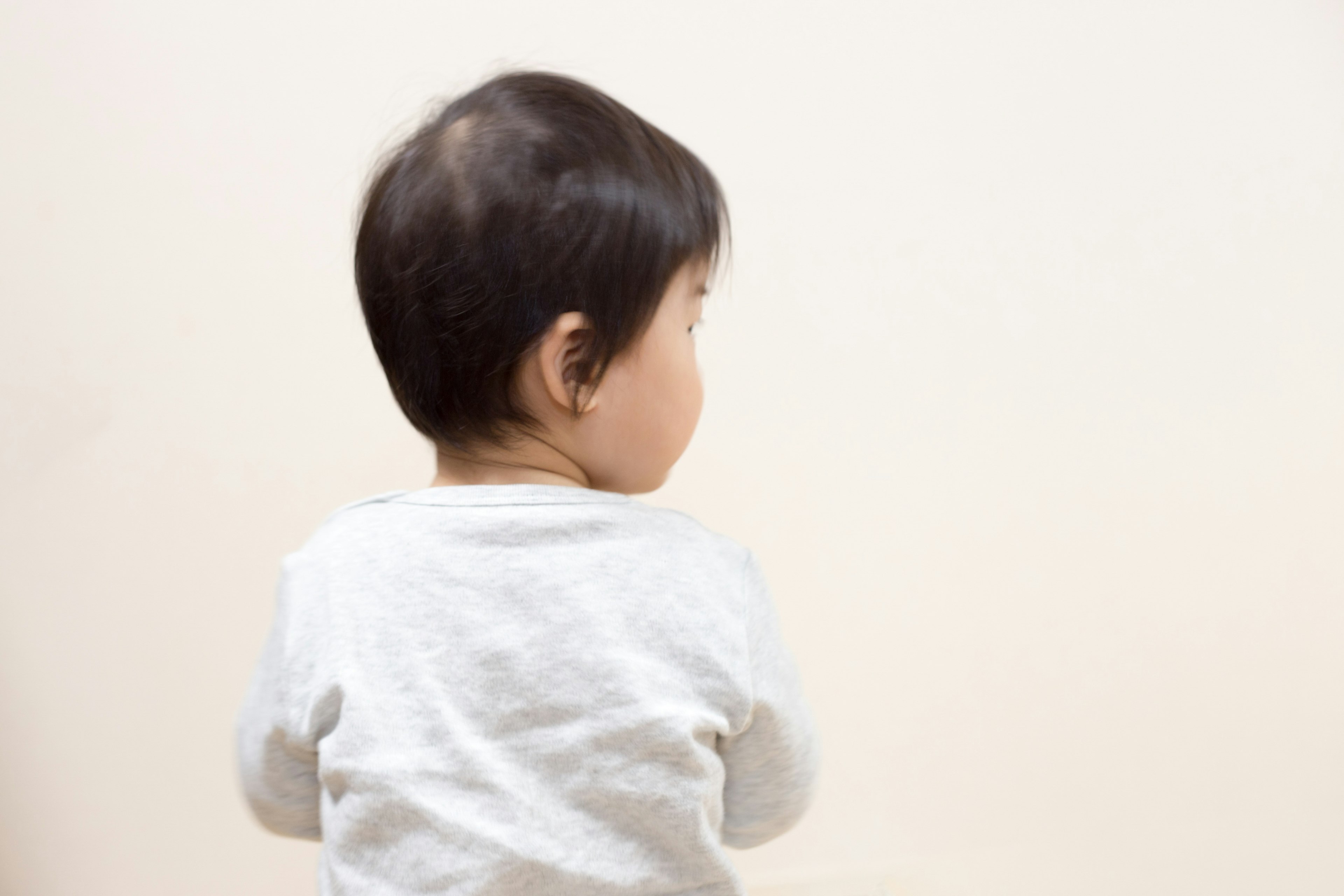 A child seen from the back with short dark hair against a light background