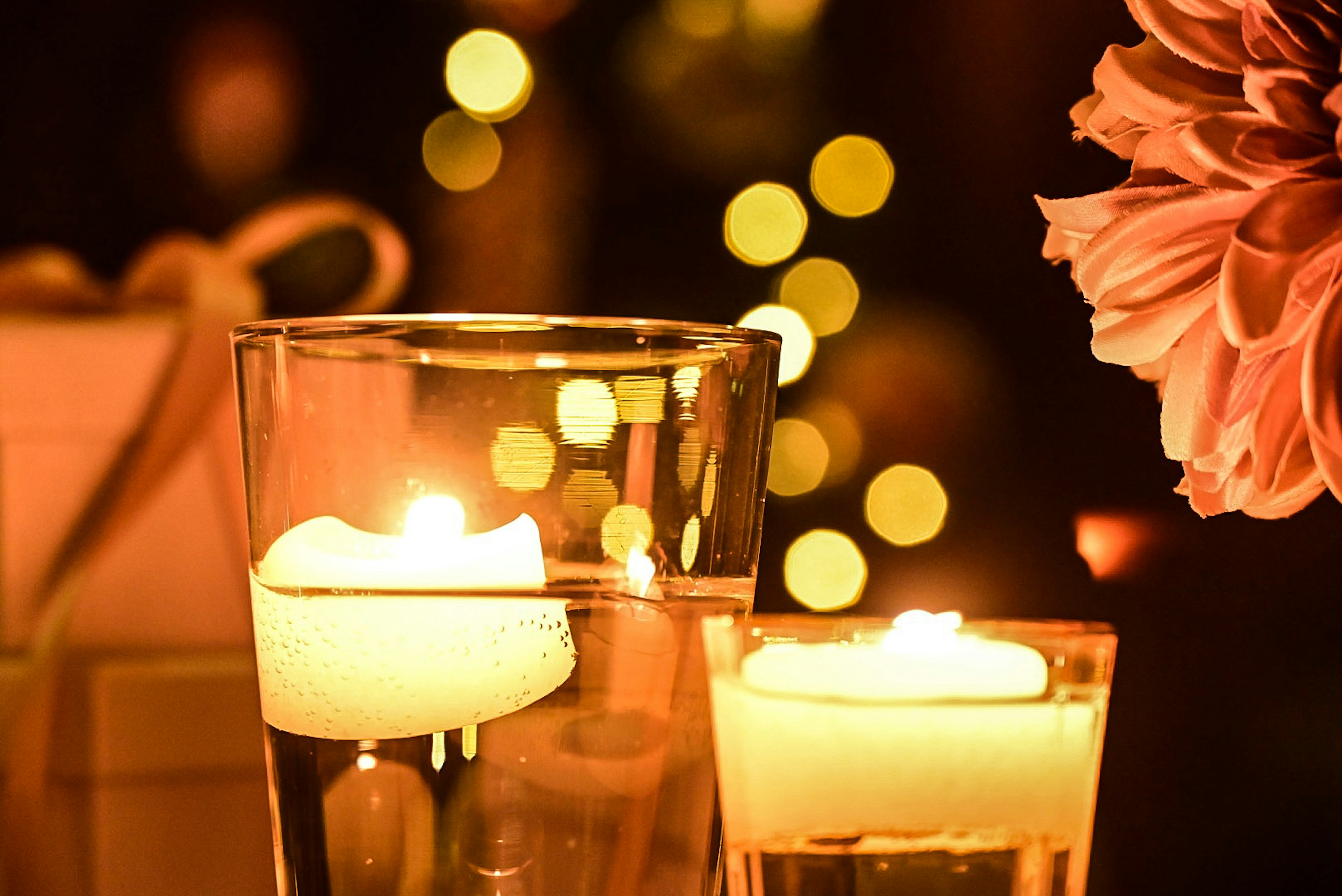 Two glass containers with floating candles and a blurred light background featuring a flower