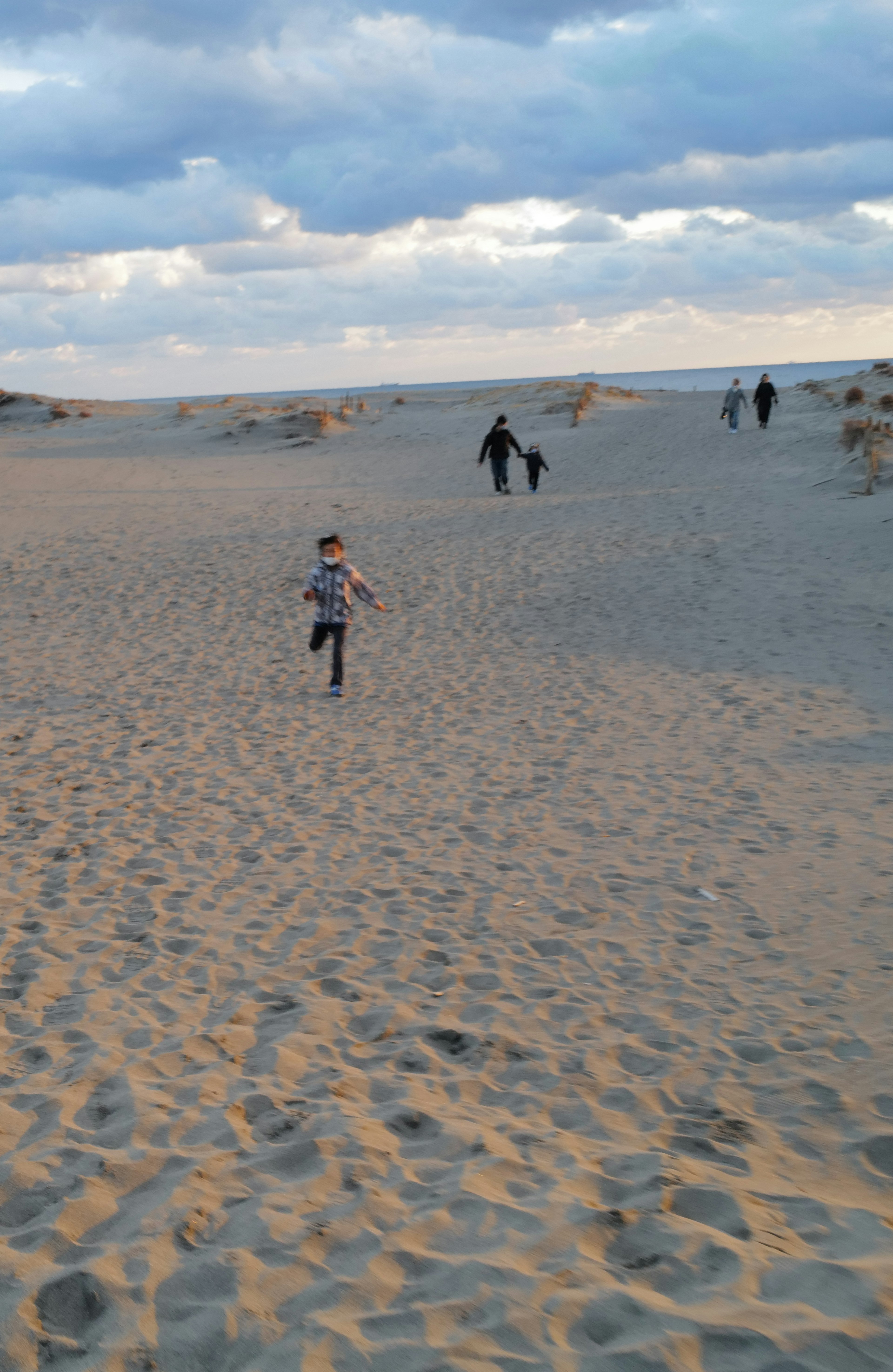 Un bambino che corre sulle dune di sabbia con persone sullo sfondo