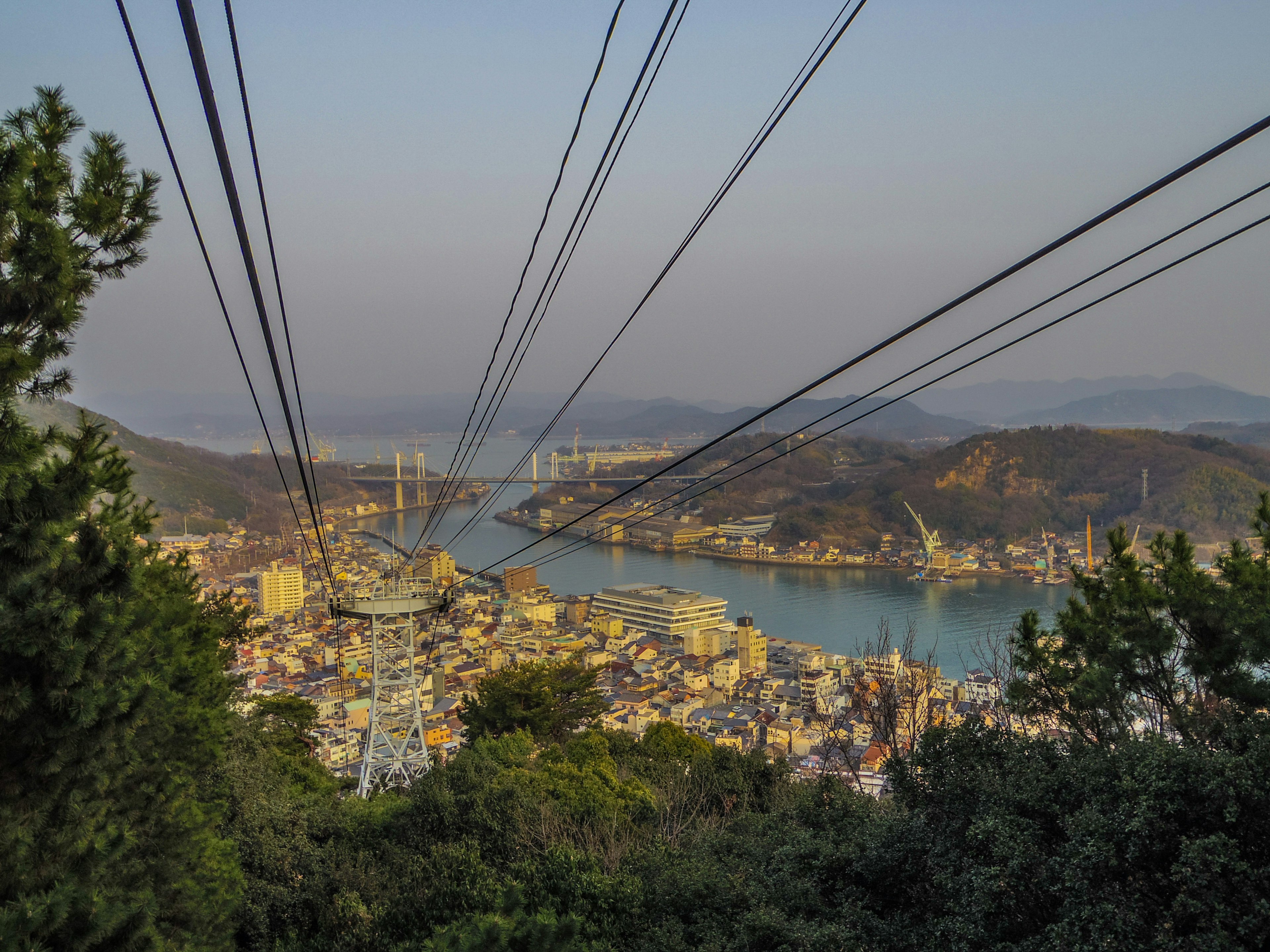 Vista escénica de una ciudad y un río desde una montaña con líneas de teleférico