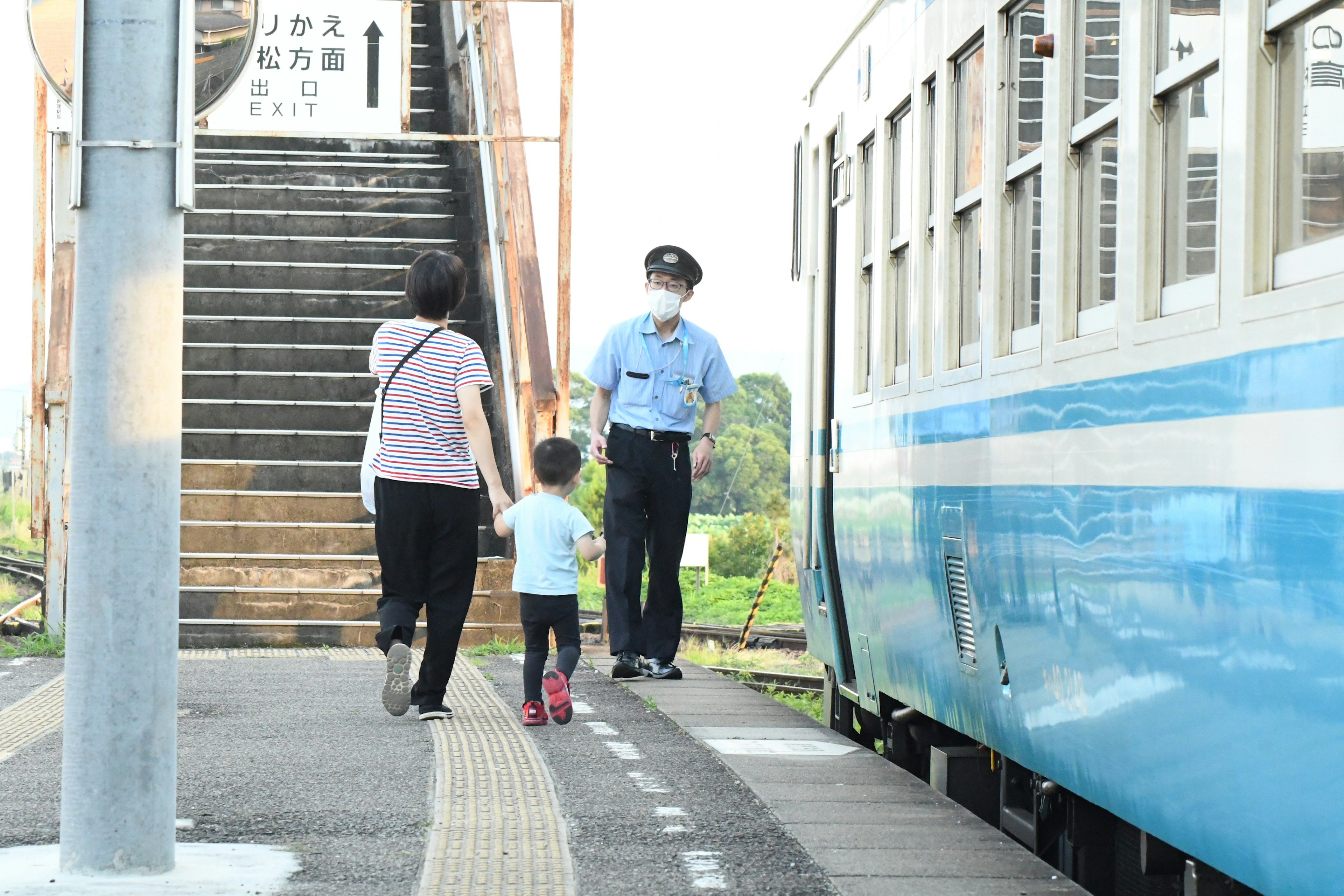 Un enfant et un parent interagissant avec un membre du personnel dans une gare de train bleu