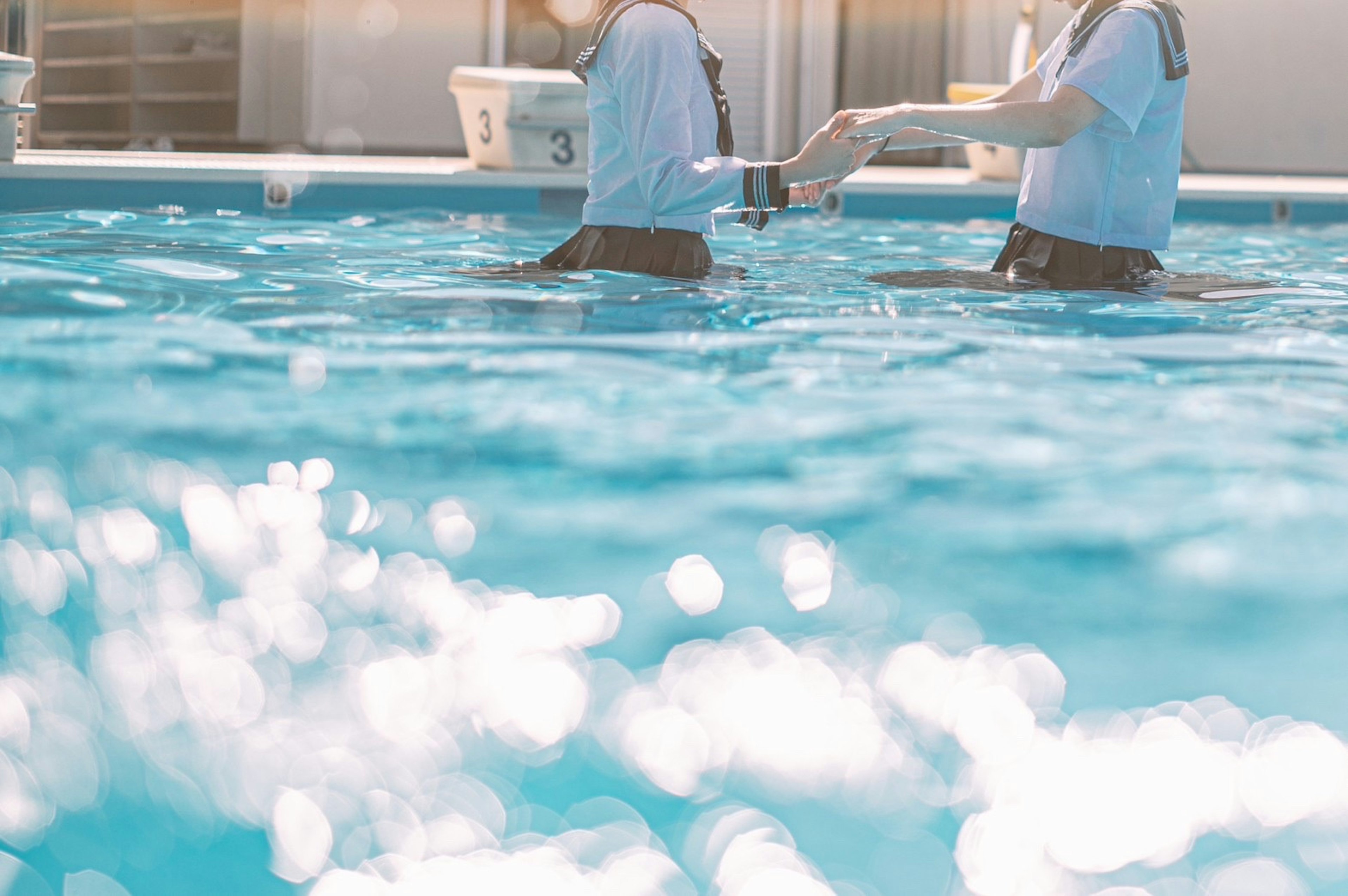 Zwei Personen halten sich in einem Pool mit leuchtend blauem Wasser an den Händen