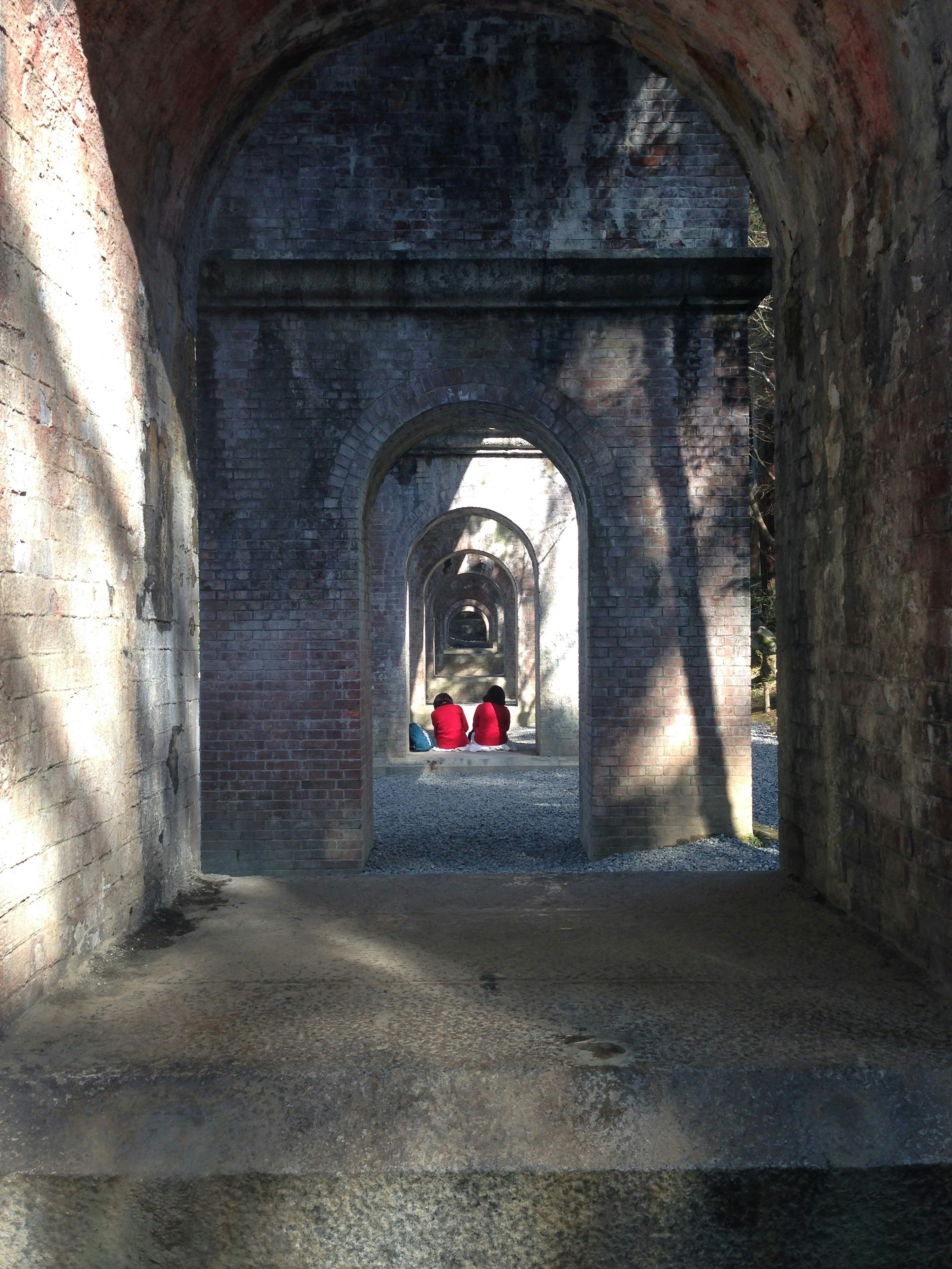 Two people in red clothing walking through an old arched tunnel