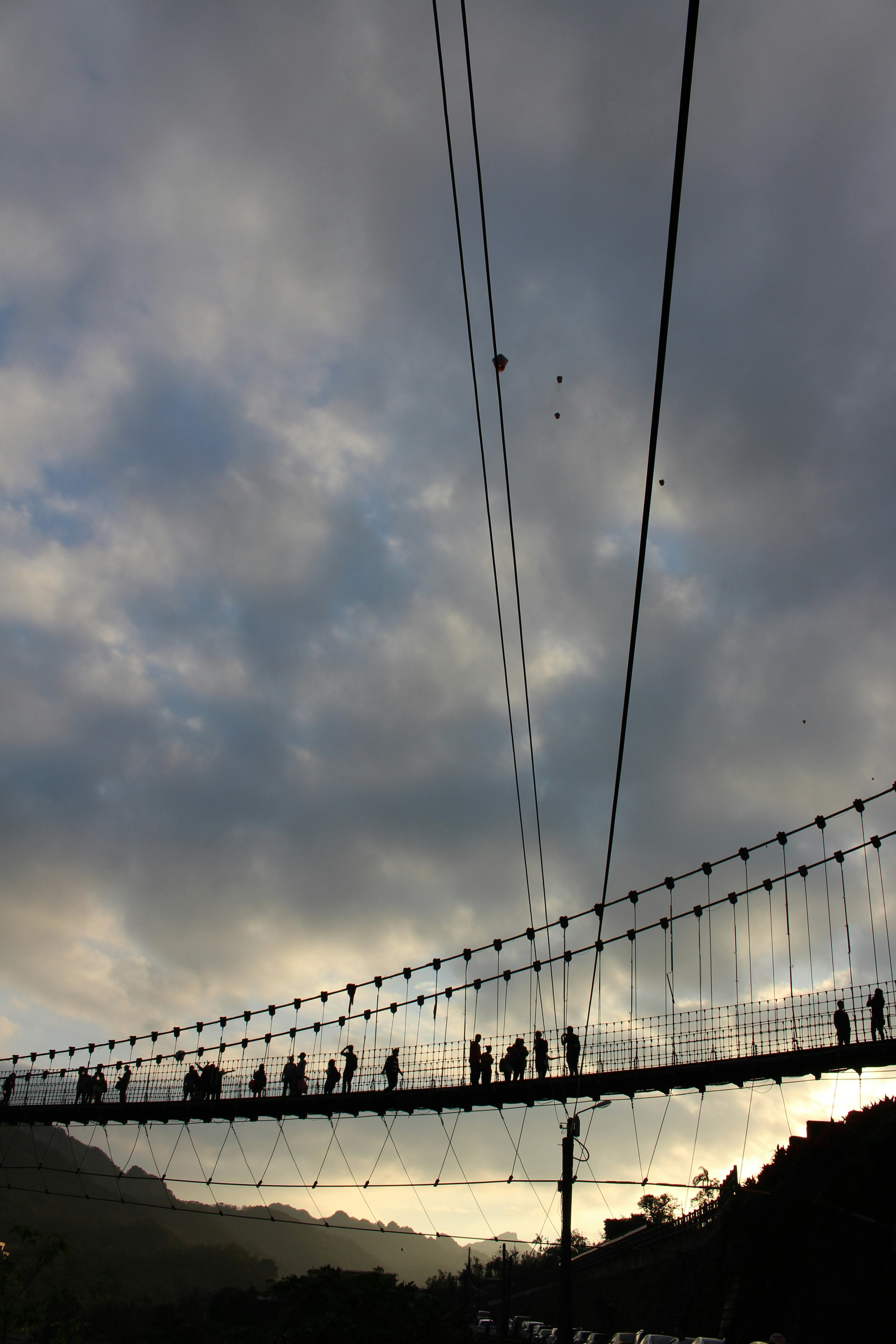 Silhouette of a bridge with people walking against a cloudy sky