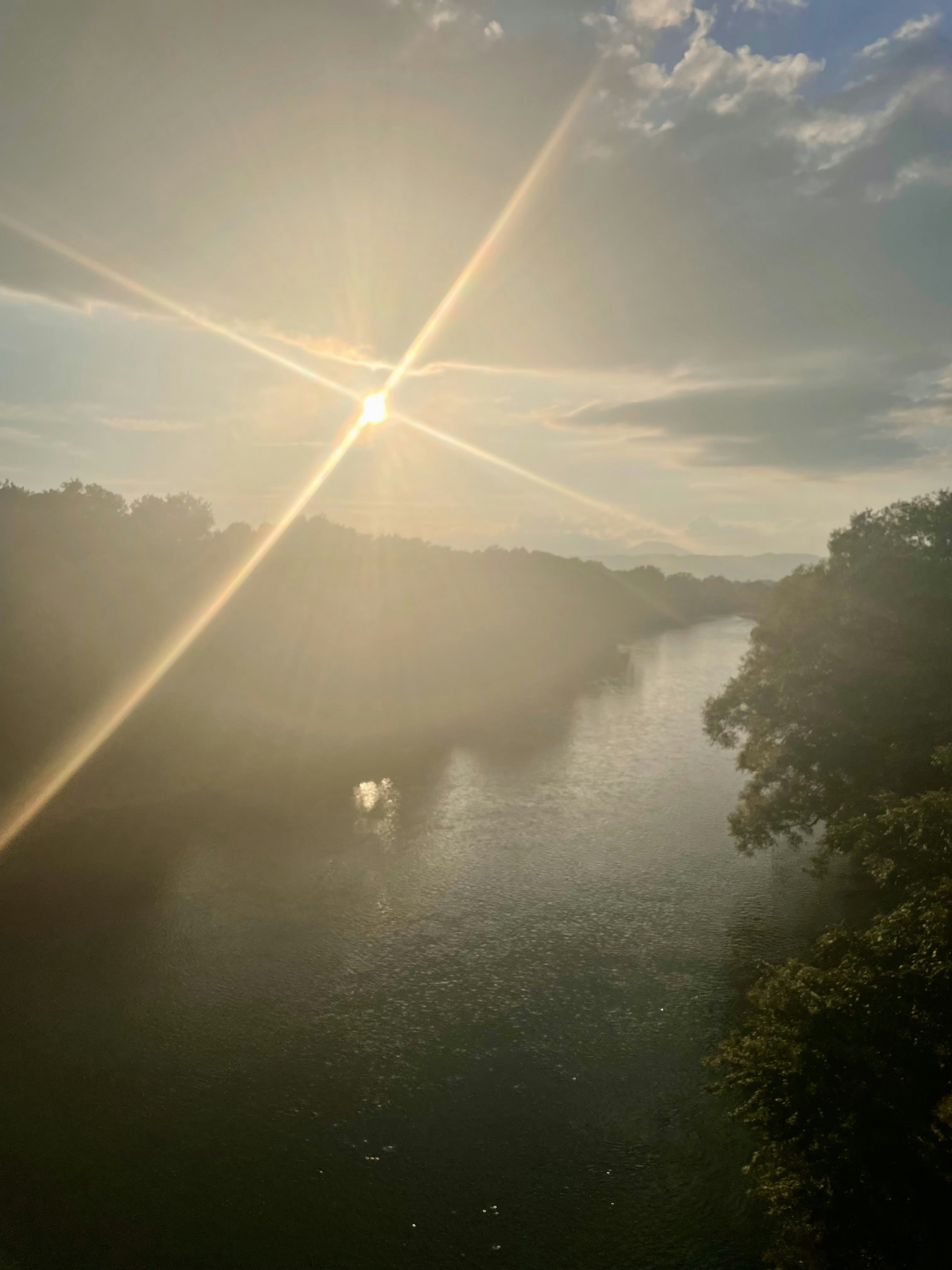 Matahari bersinar di atas sungai dengan pohon di latar depan