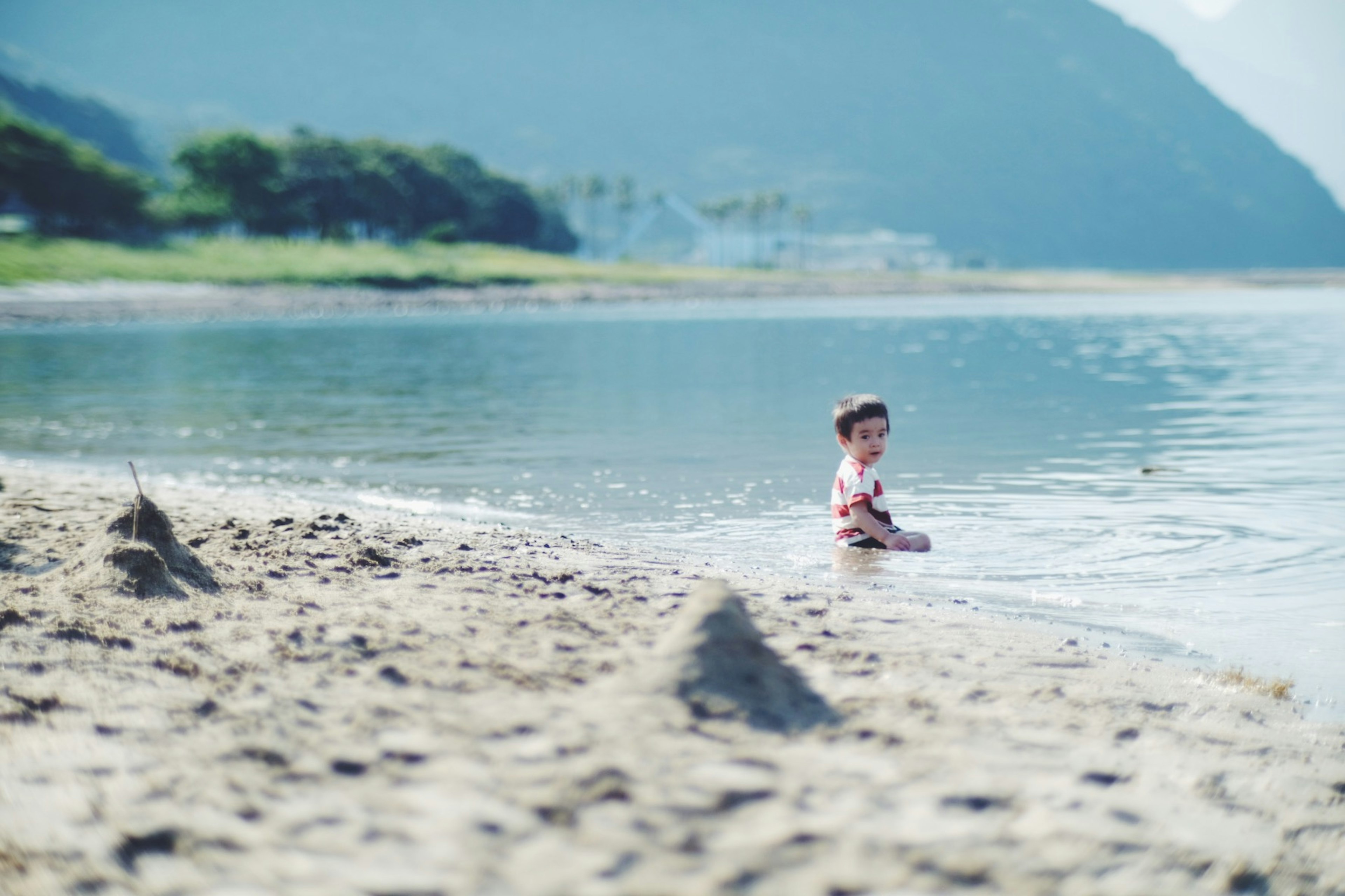 Anak bermain di pantai dengan gunung dan air biru di latar belakang