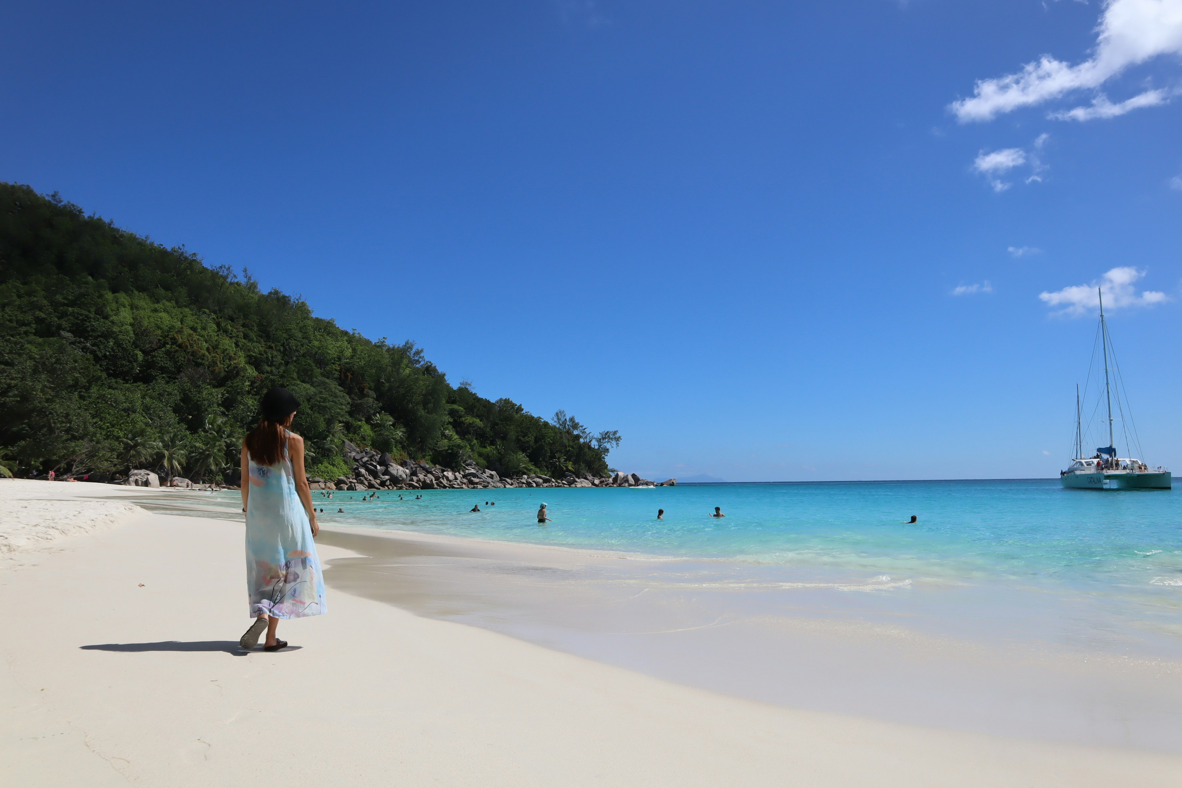 A woman walking along a white sandy beach with clear blue water