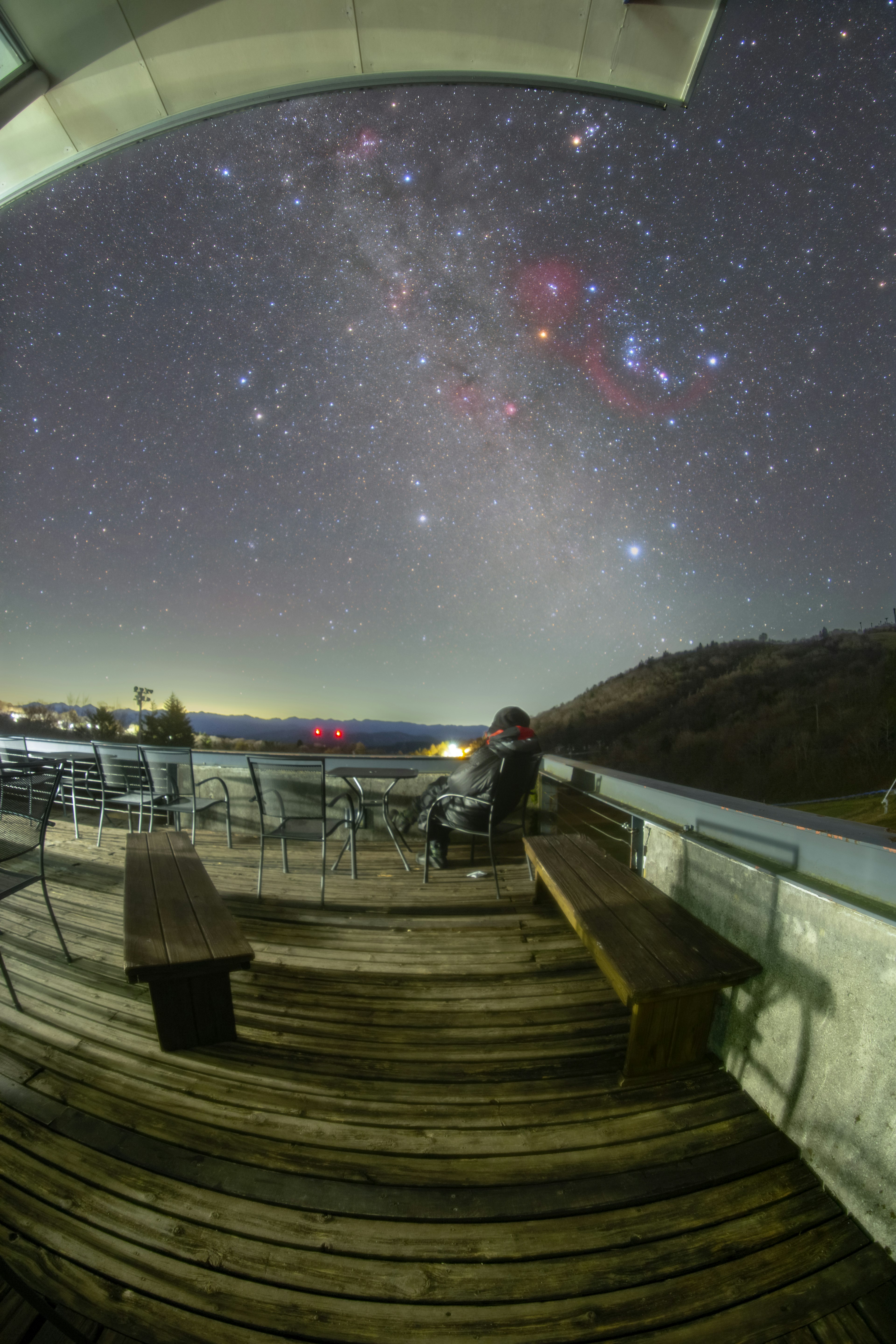 星空の下、テラスに座っている人物と木製のベンチが見える夜景